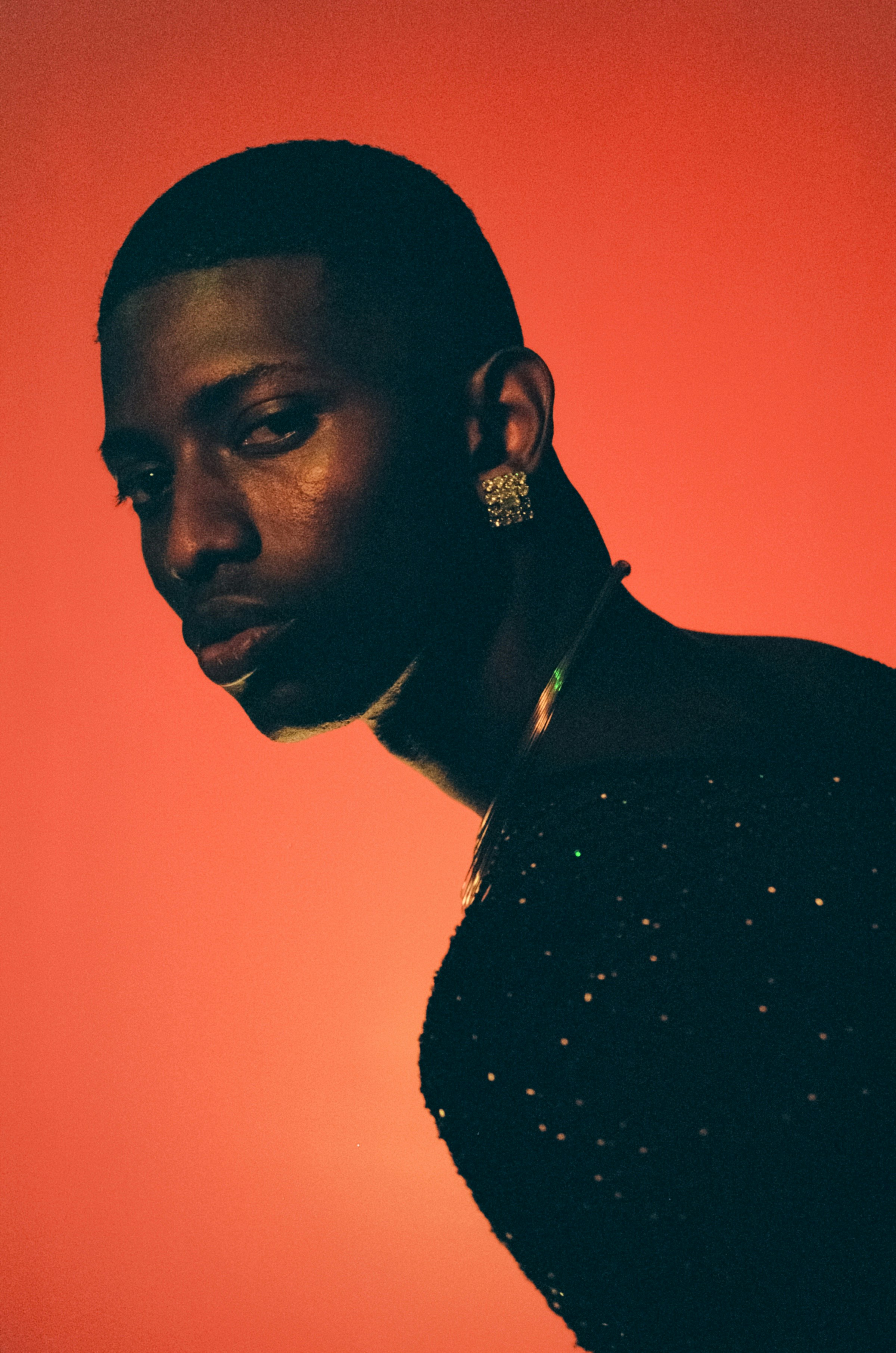 A person with short hair and a sparkling earring against a vibrant orange background