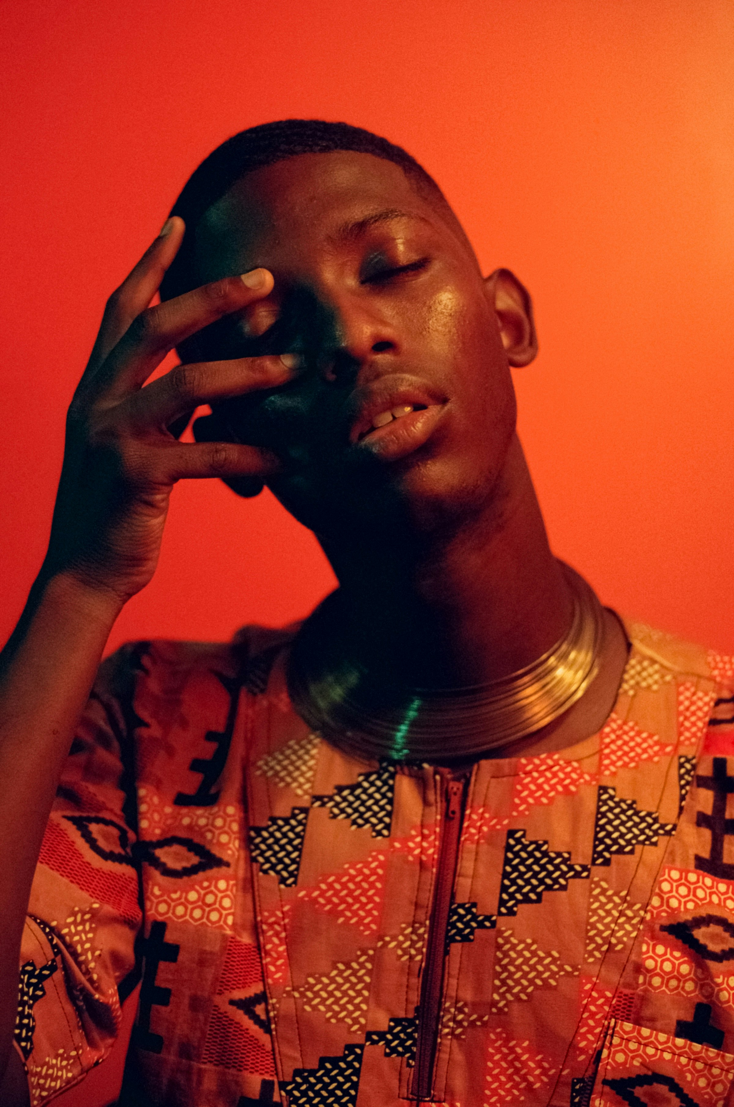 Hand at the brow, patterned shirt and metal collar