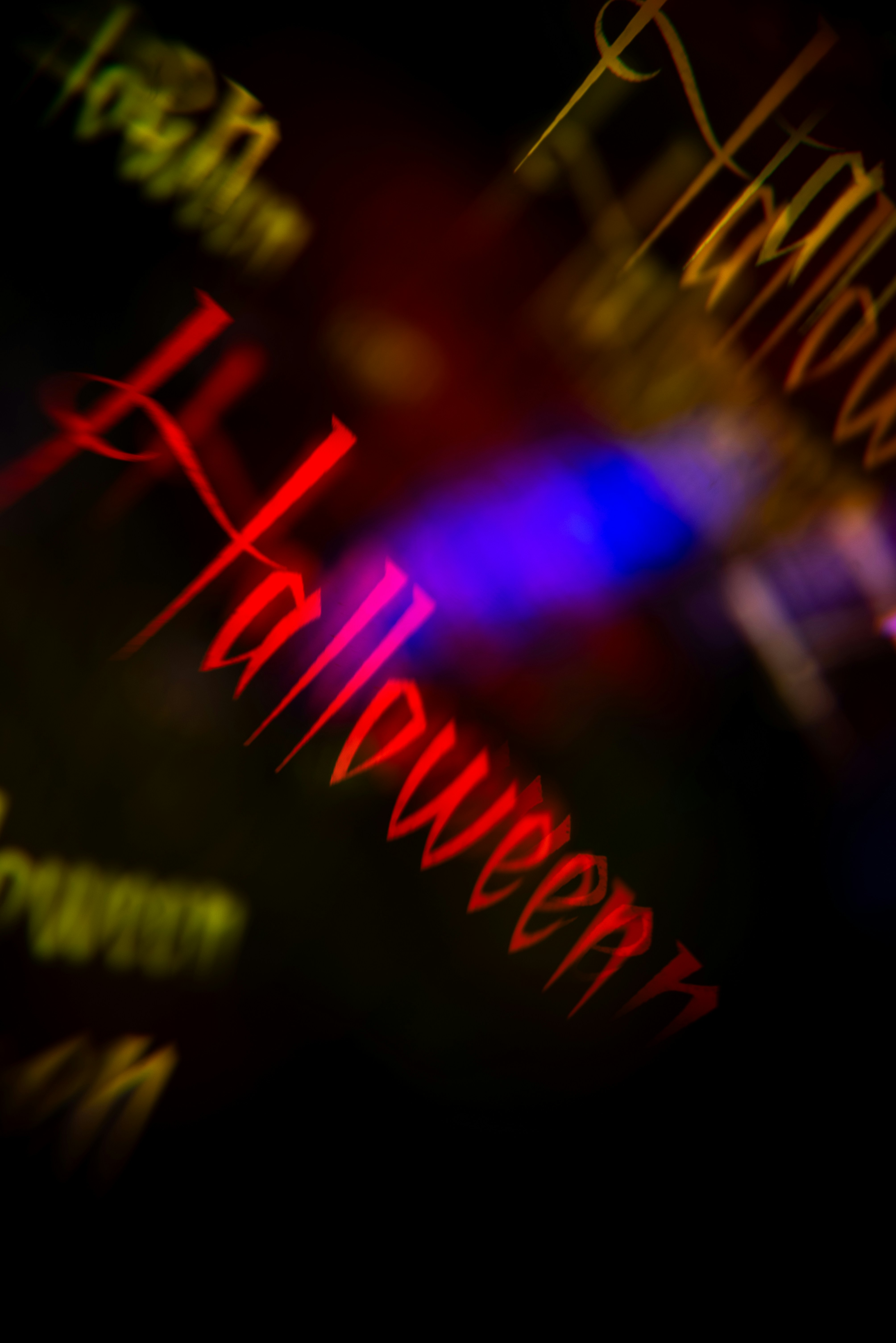 Le mot Halloween en lettres gothiques rouges sur fond sombre avec une lumière floue bleue et jaune