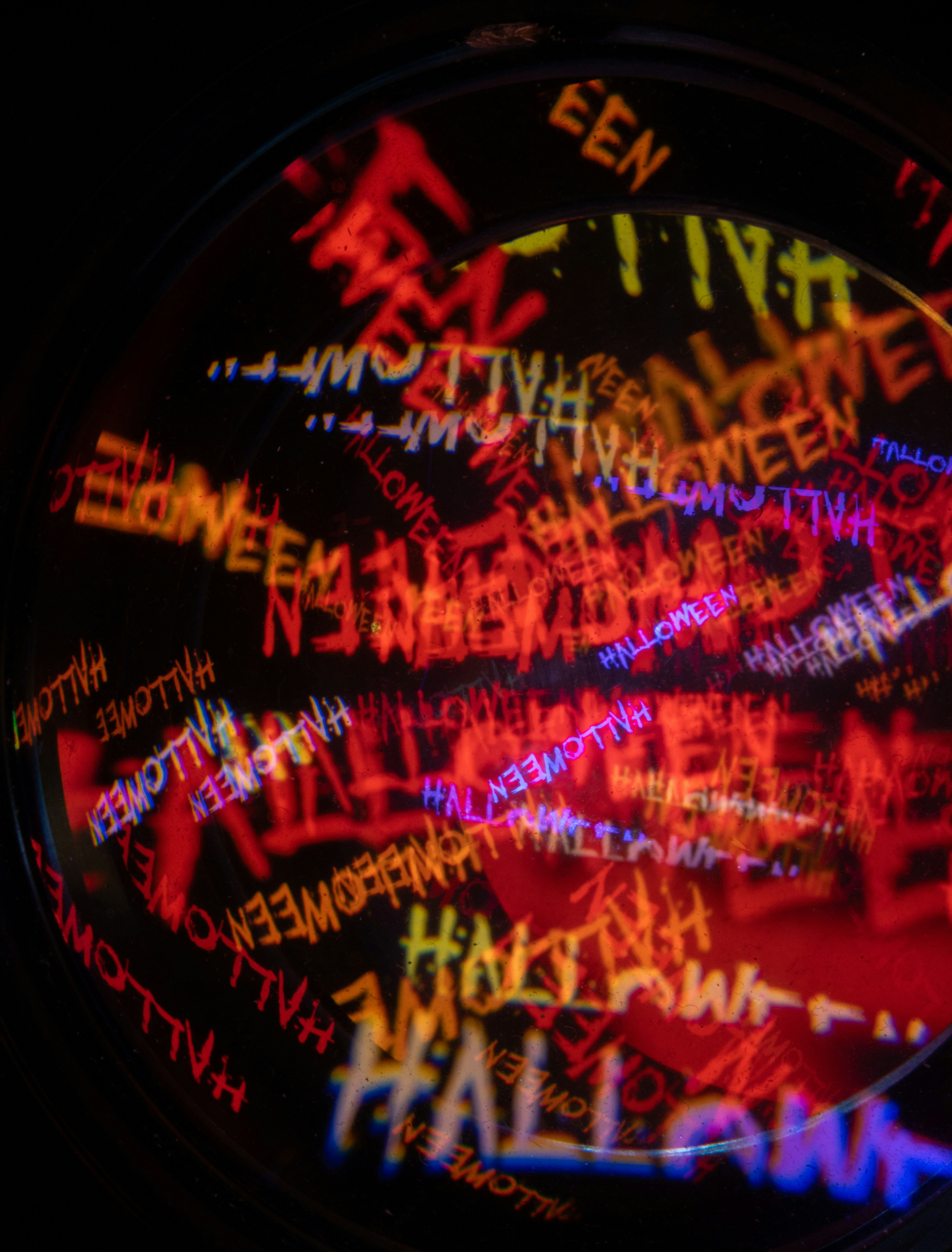 Multiples reflets superposés du mot Halloween dans des lumières néon rouge, jaune et bleue