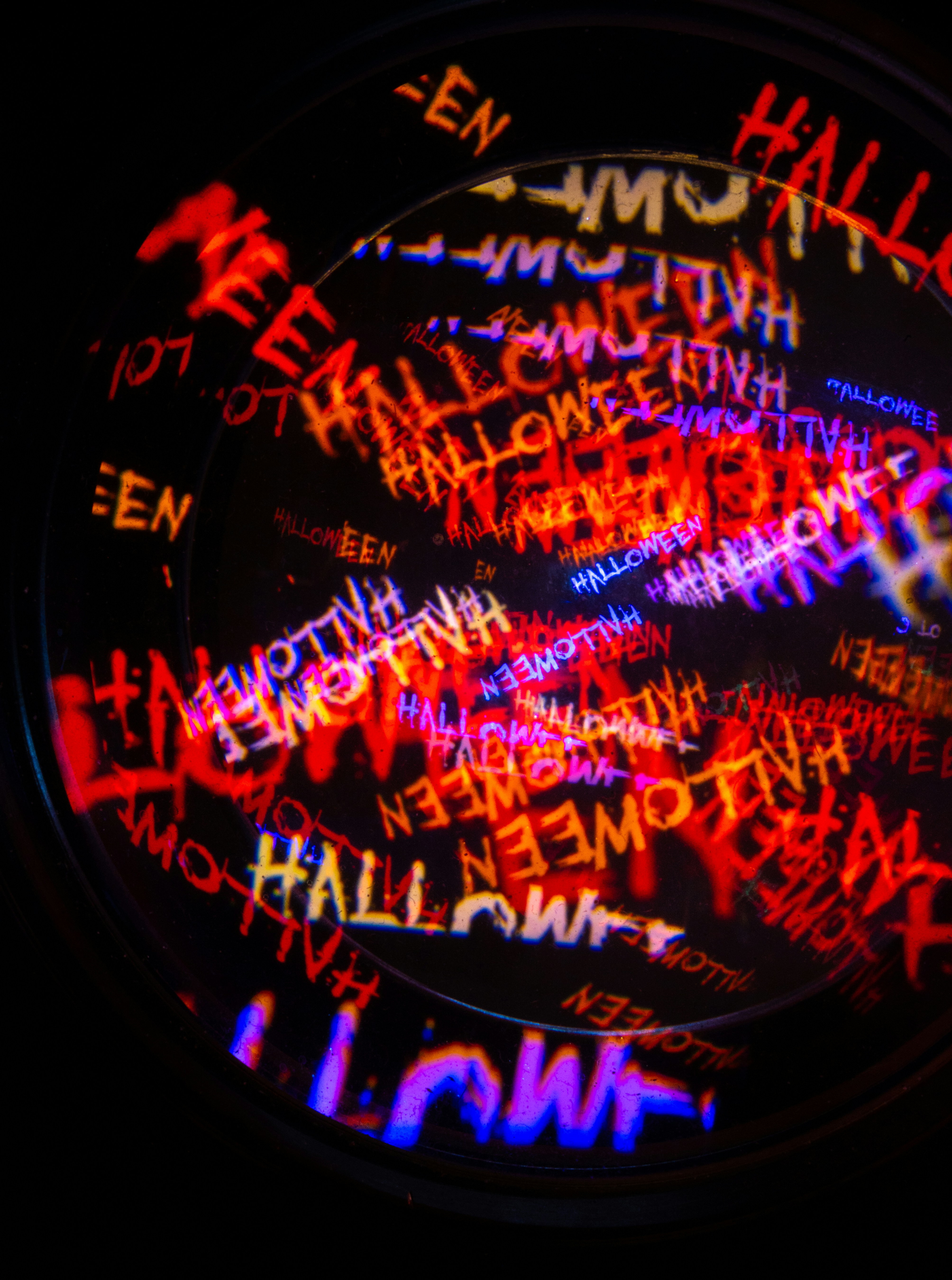 Plusieurs projections superposées du mot Halloween en rouge, orange et bleu sur un fond sombre