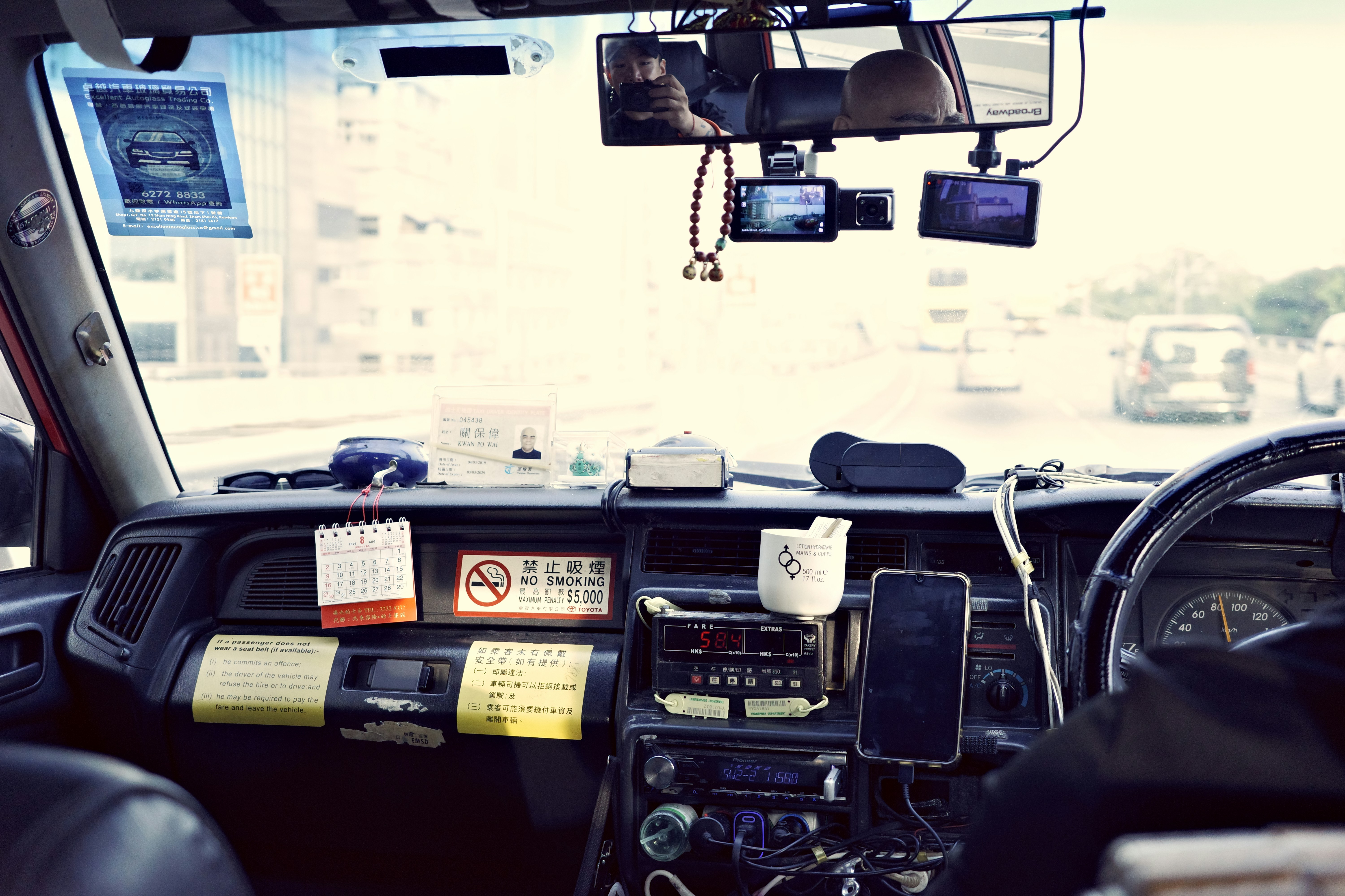 The interior of a taxi dashboard with a fare meter, phone, and various signs in Hong Kong