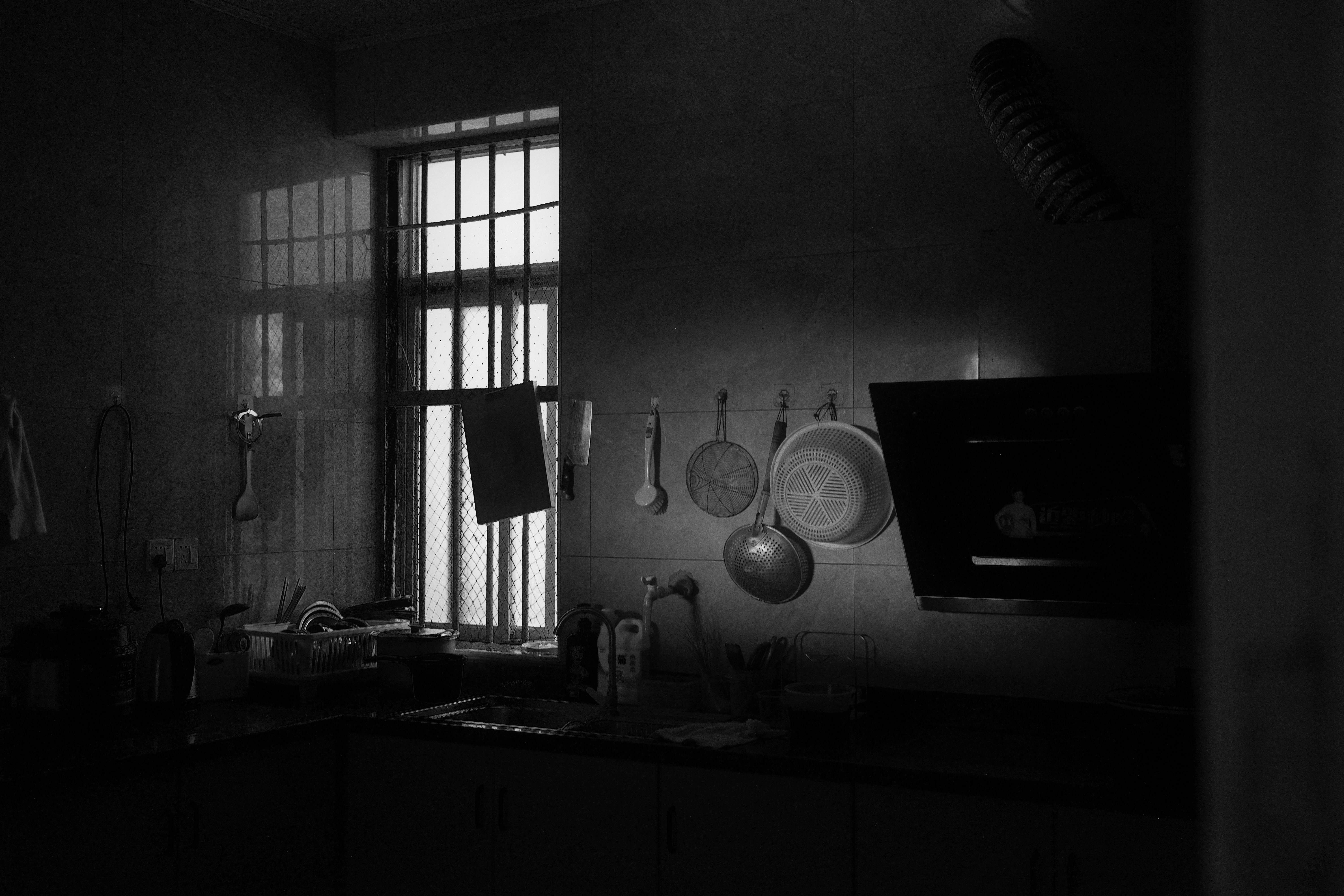 A dimly lit kitchen with hanging utensils and a window casting long shadows