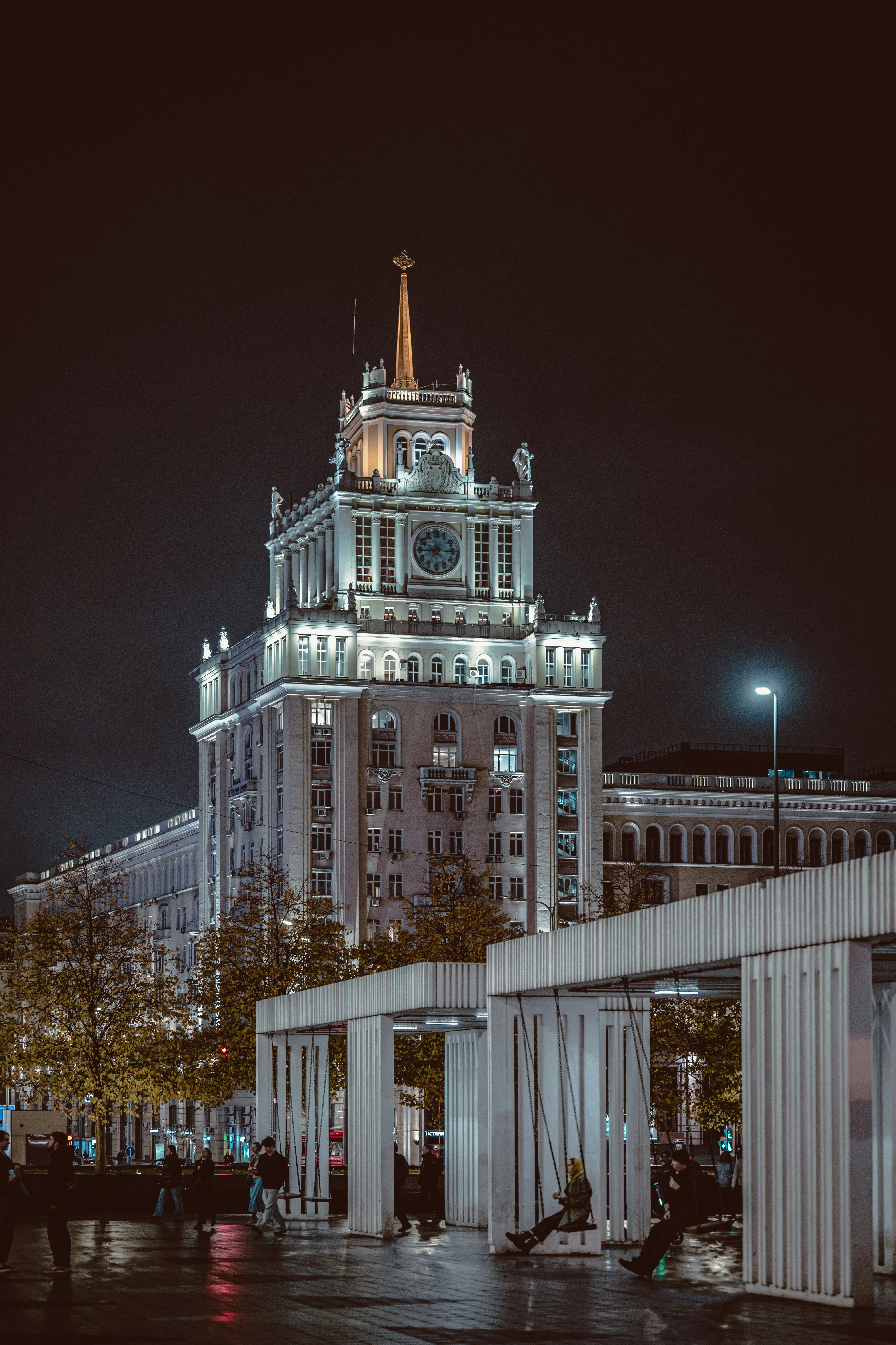 Gedung Triumph Palace yang diterangi di malam hari dengan orang-orang di ayunan di latar depan