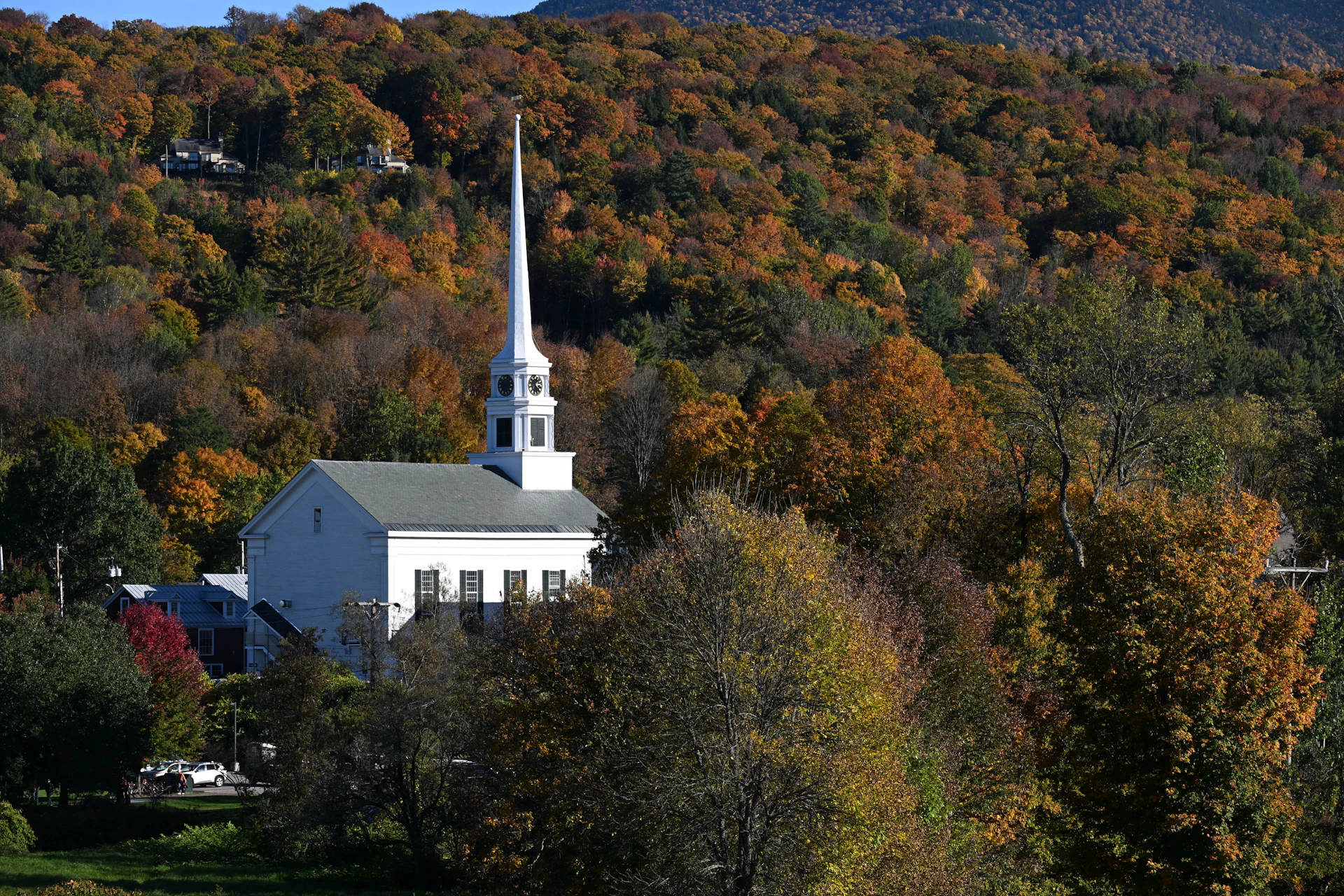 A white church with a tall steeple nestled in a forest of autumn trees