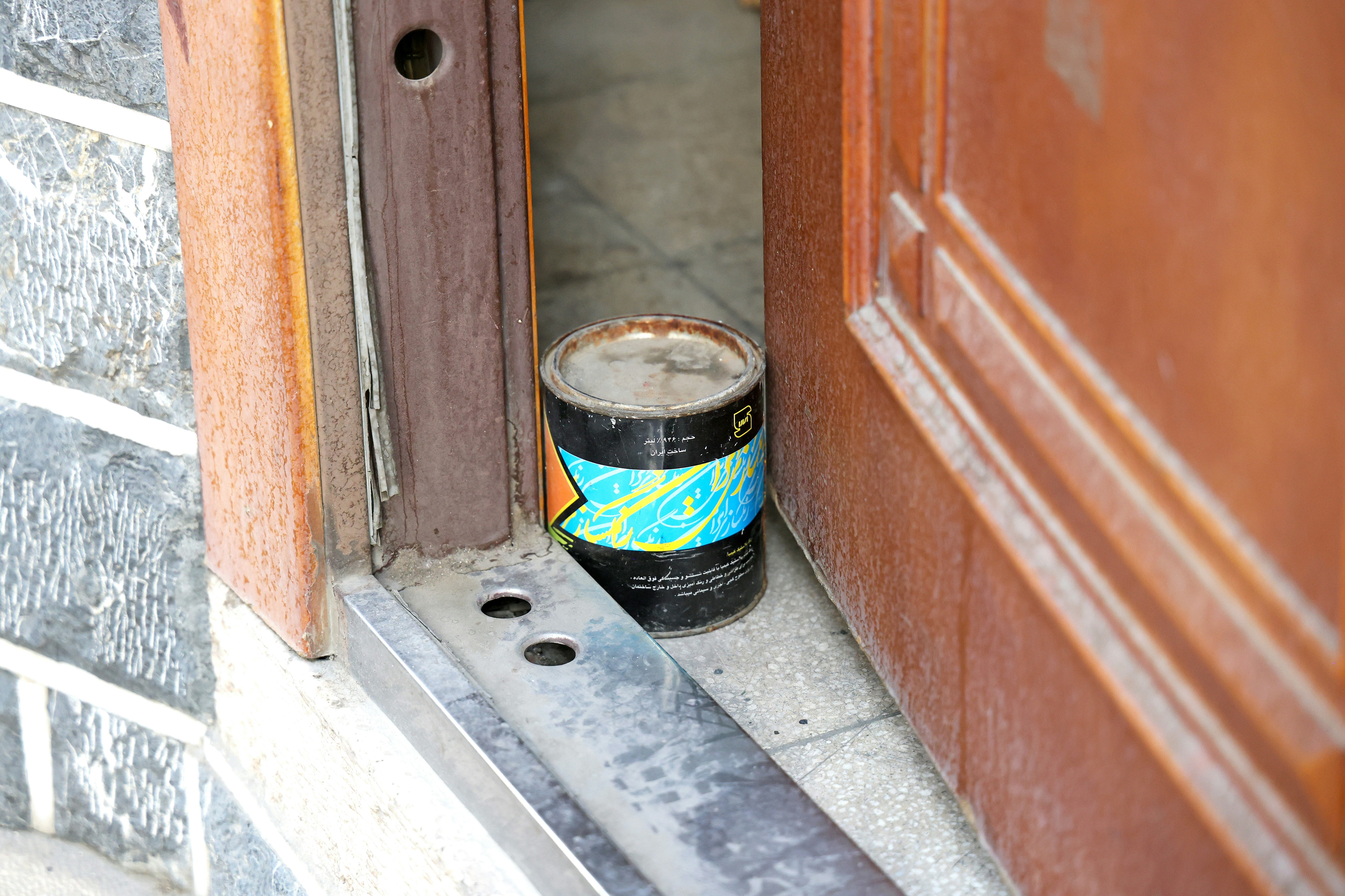 Soleira metálica na base de uma porta de madeira entreaberta, com uma lata de tinta no chão