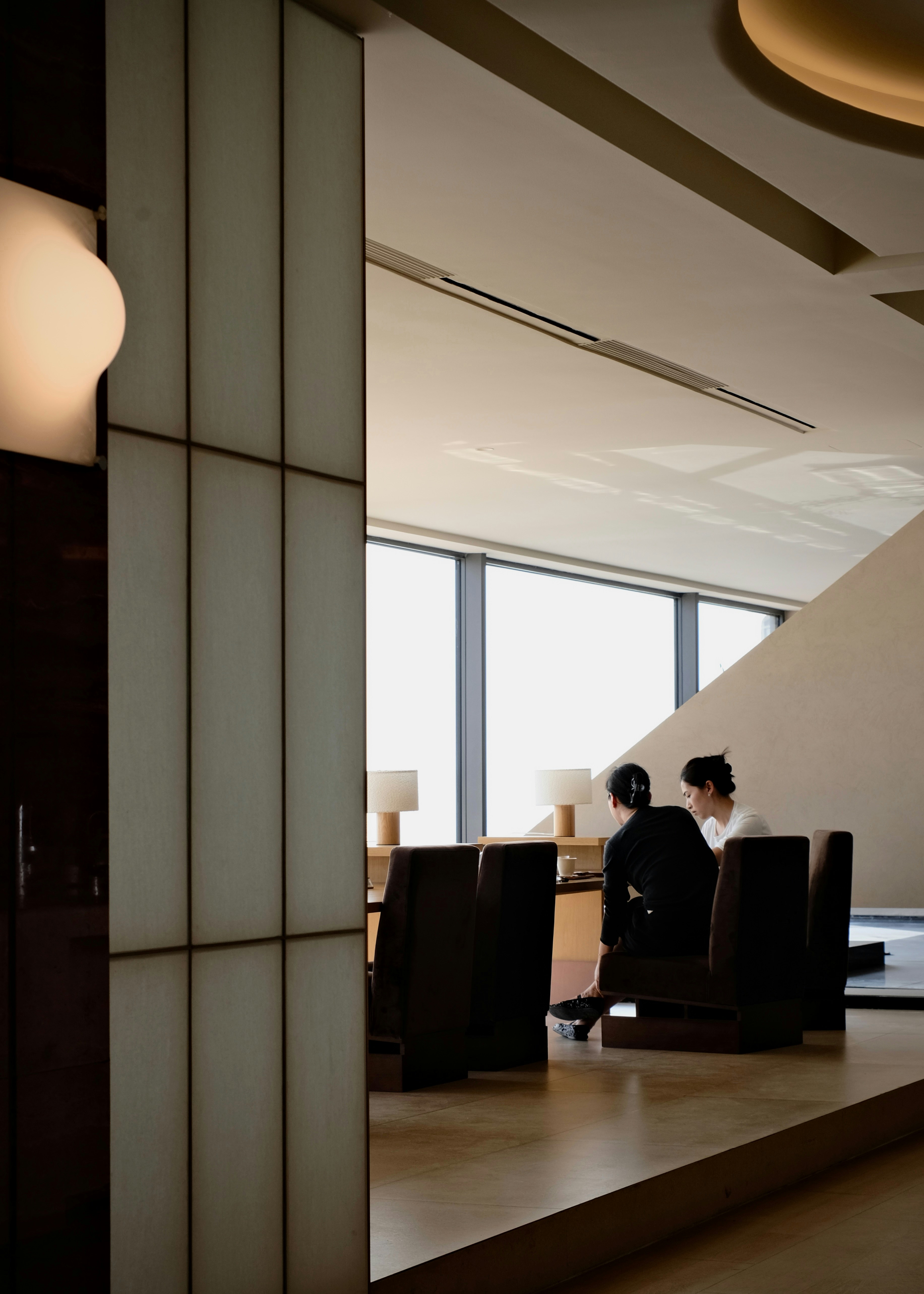 Two people sitting at a table in a minimalist sunlit room with large windows