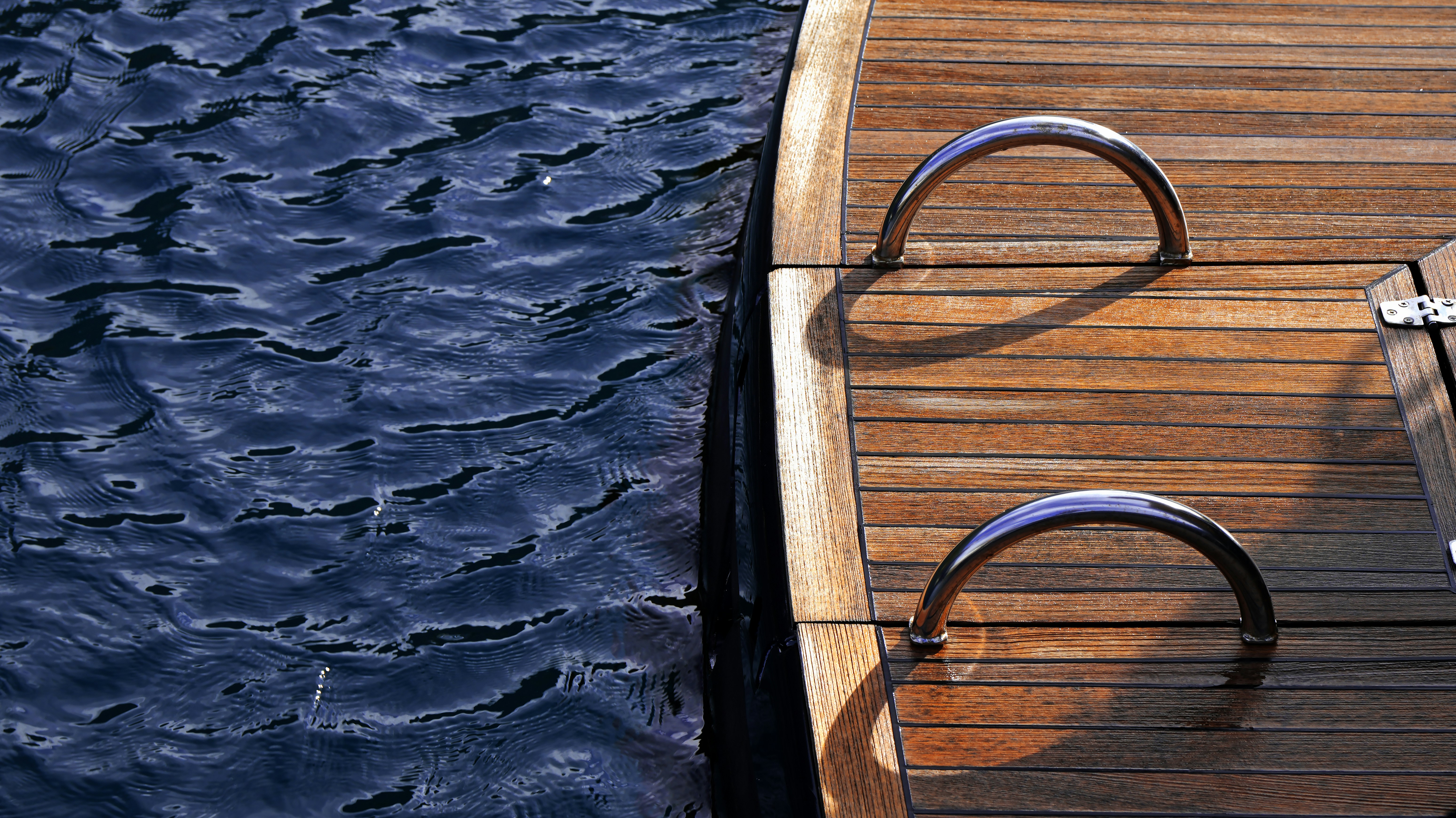 Stainless steel ladder on a wooden boat deck beside dark rippling water