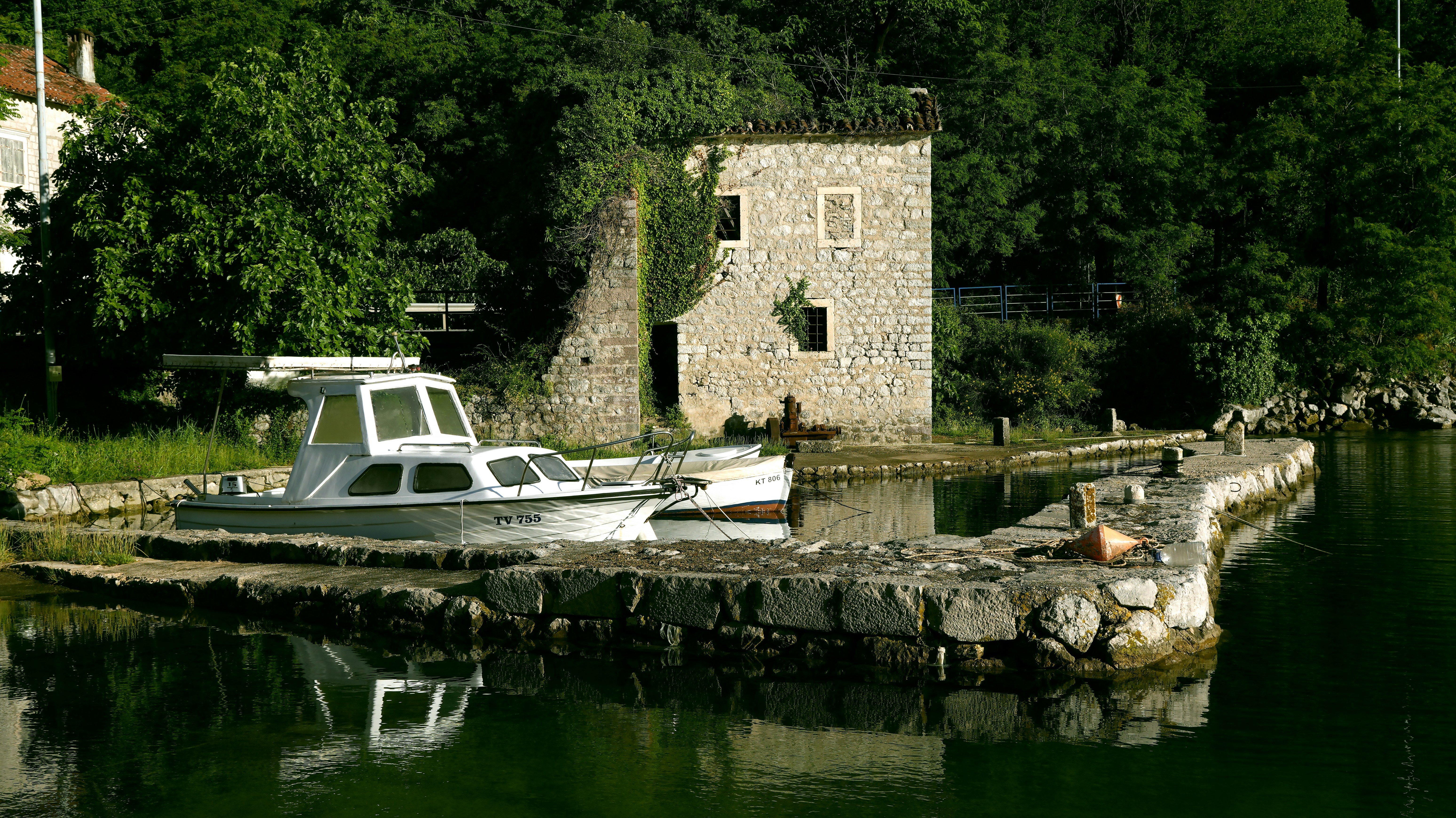 A white motorboat moored at a stone pier beside an old ivy-covered stone building