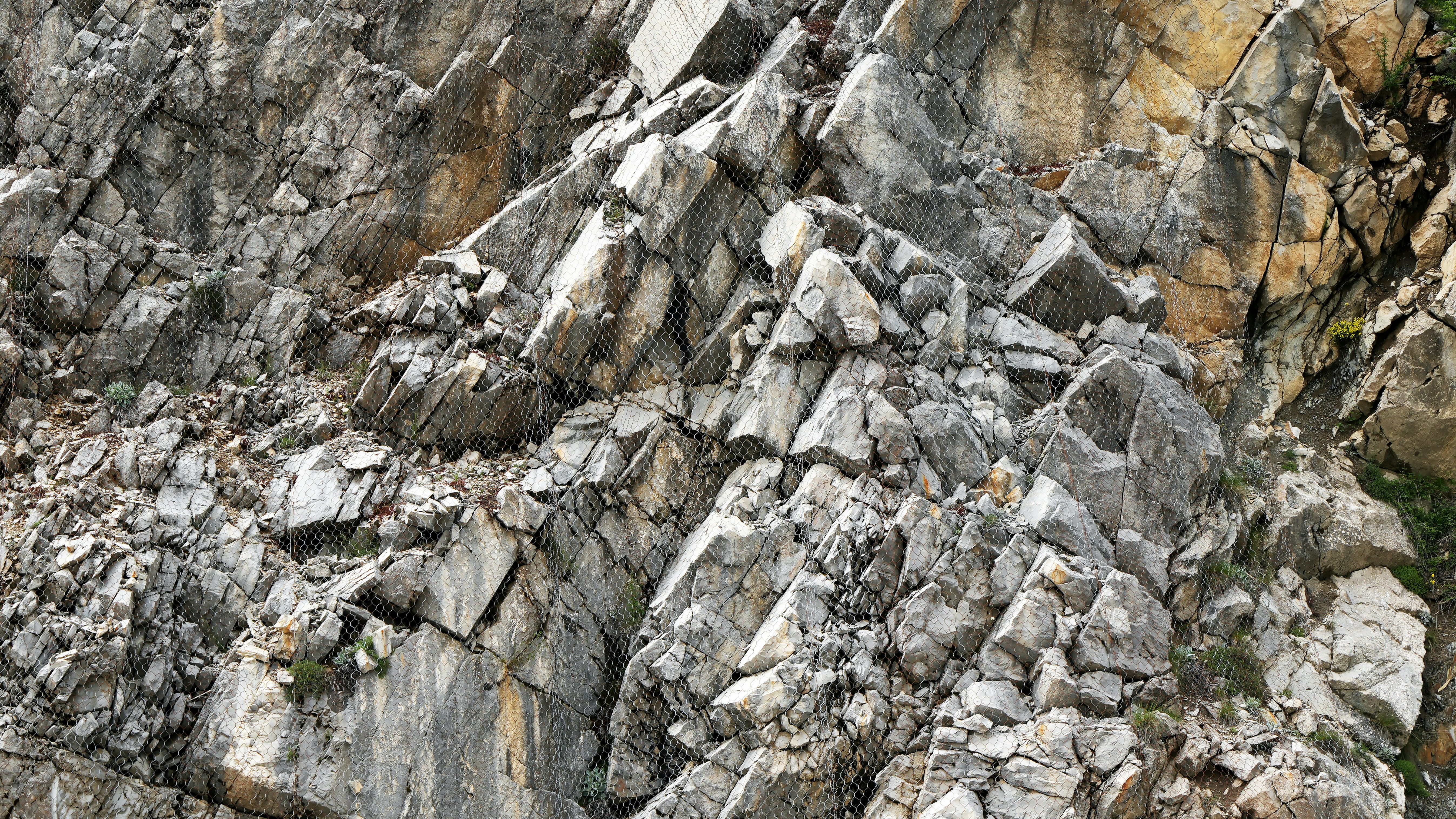 A steep rocky cliff face covered with a protective metal wire mesh netting