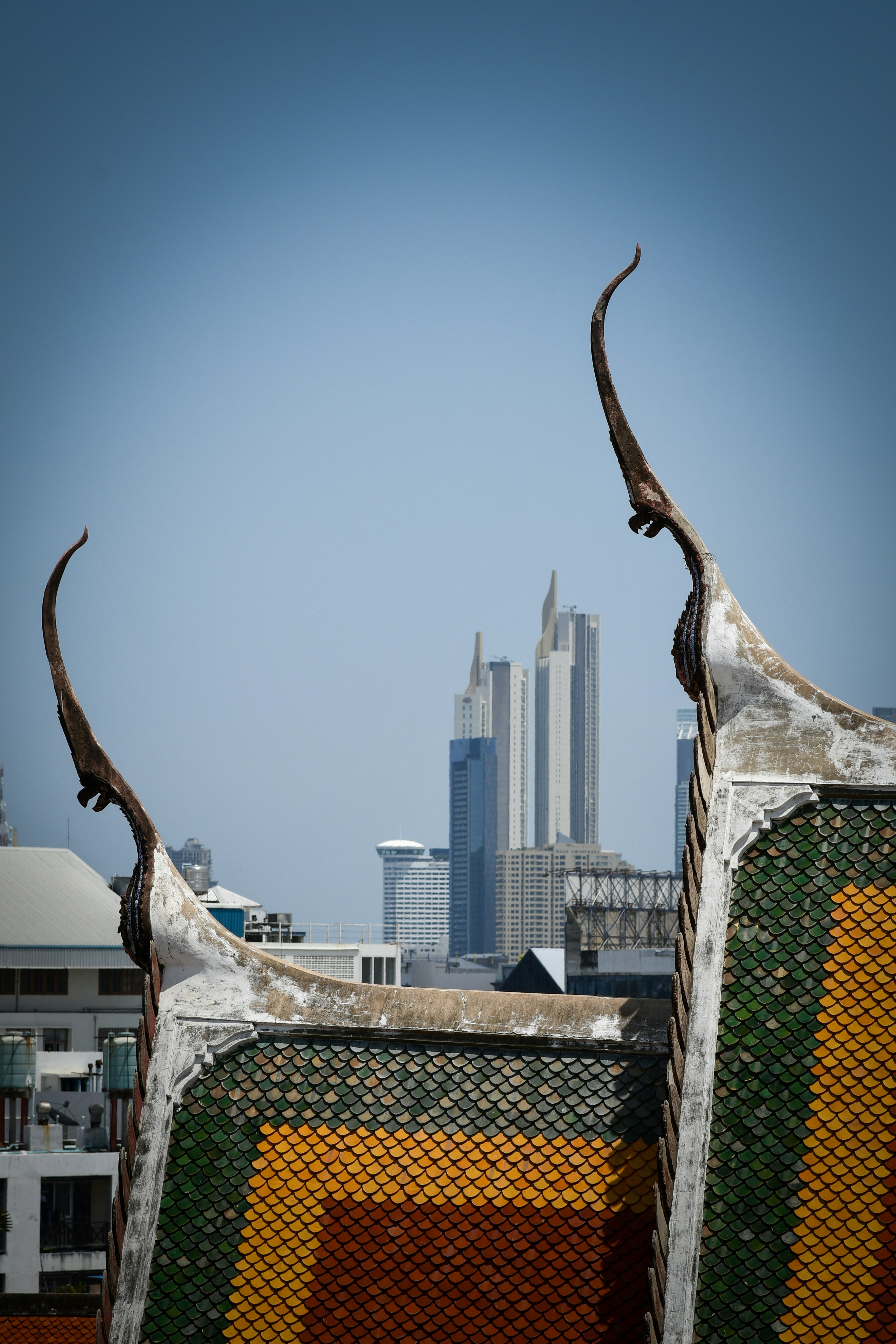 Tetto tradizionale di tempio thailandese con frontoni curvi che incorniciano lo skyline moderno di una città a Bangkok