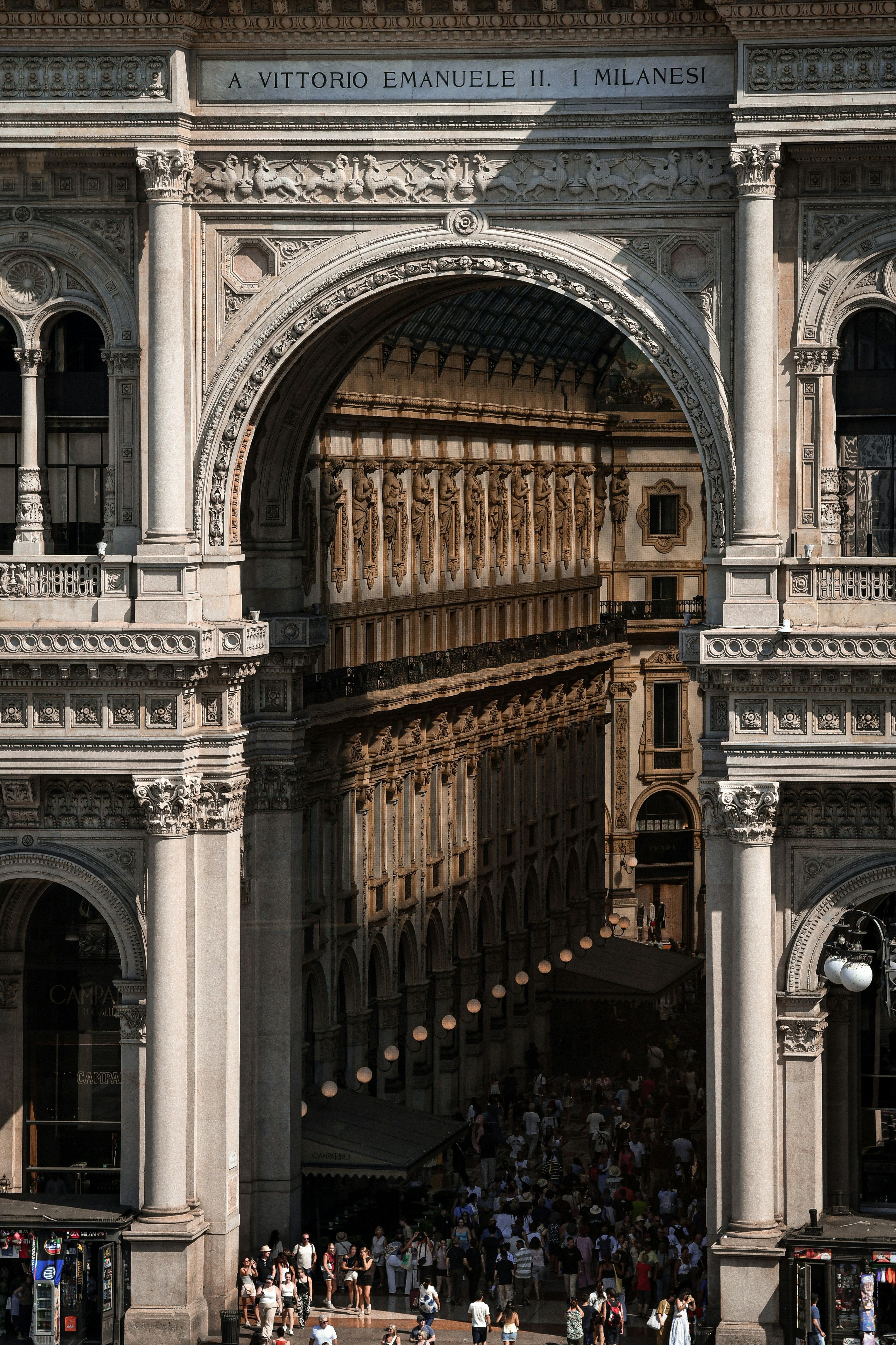 L'ornato arco in pietra della Galleria Vittorio Emanuele II a Milano con una folla di persone sottostante