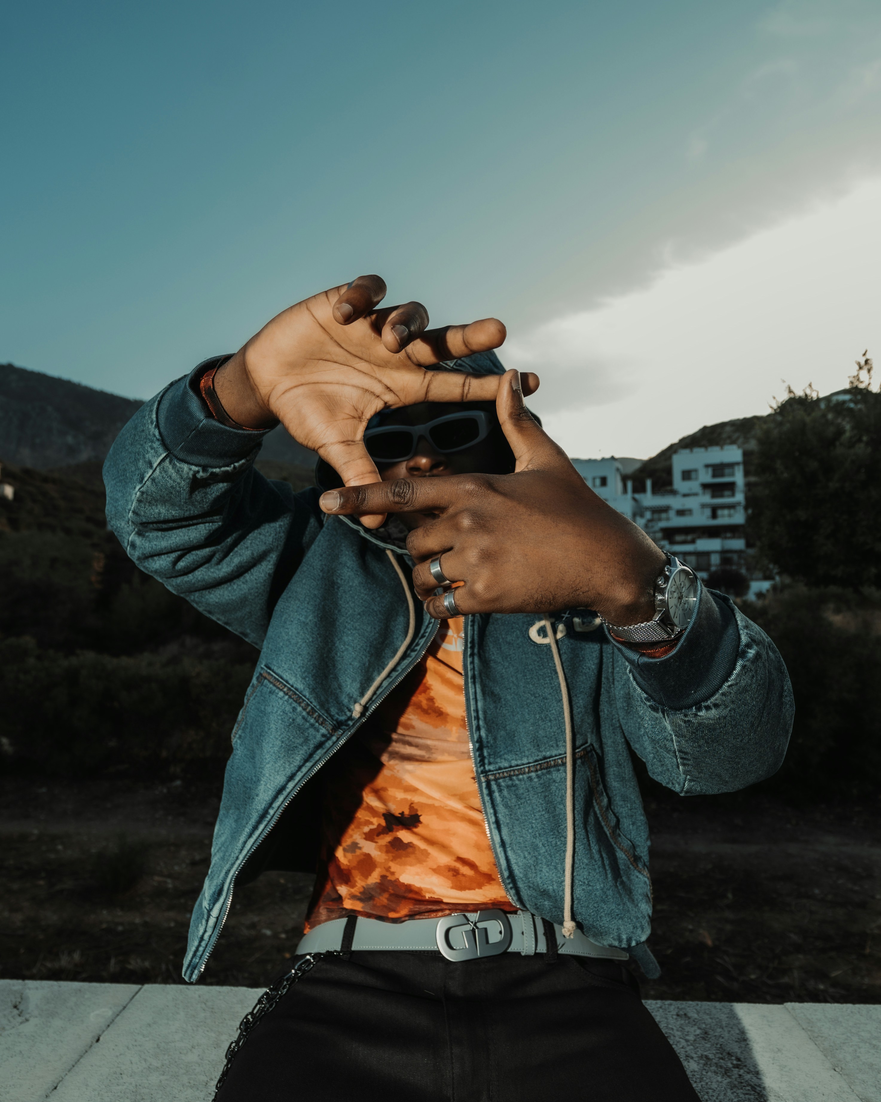A person in a denim jacket making a frame with their hands outdoors