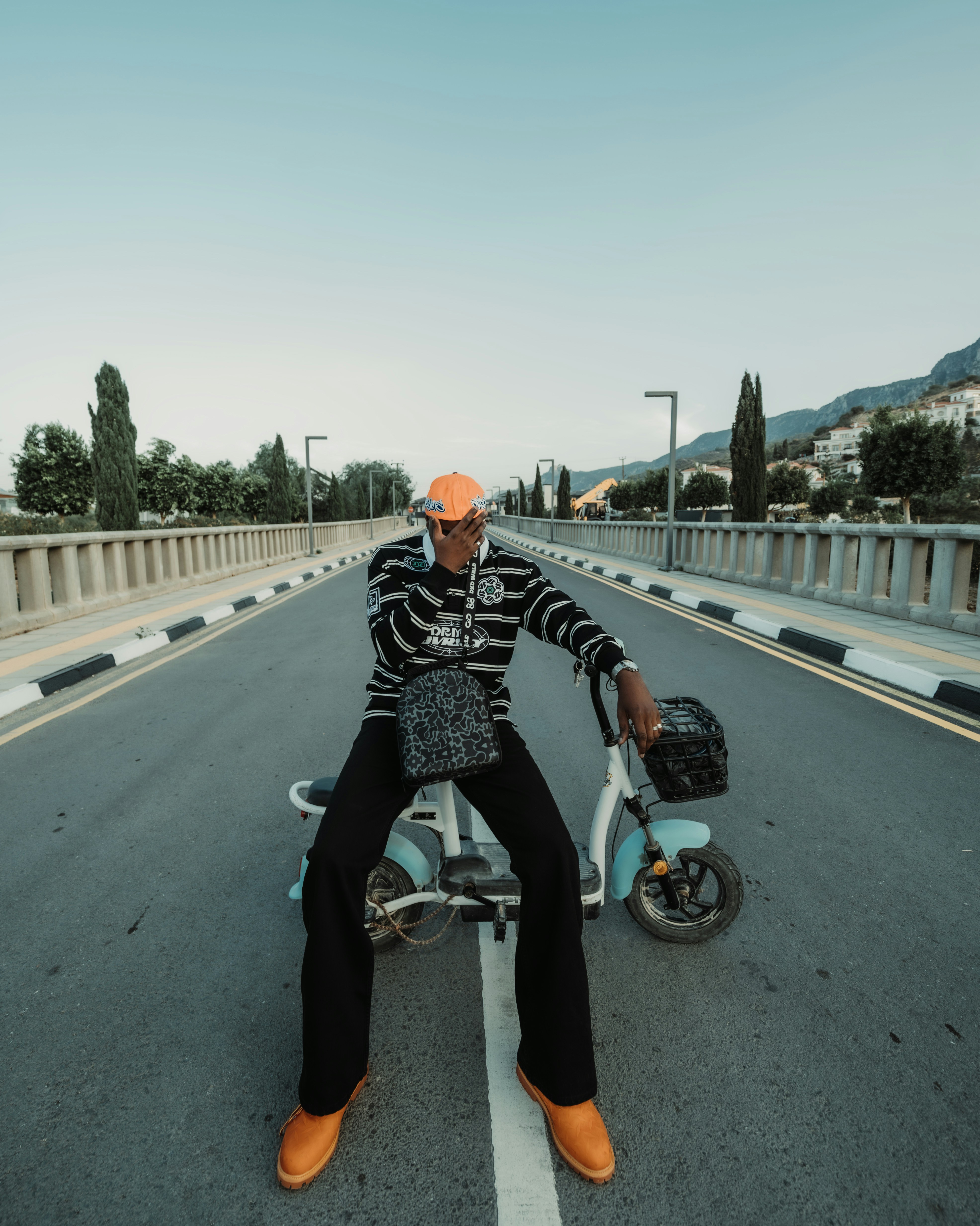 A person in a striped sweater and orange cap sitting on a small electric scooter on a bridge
