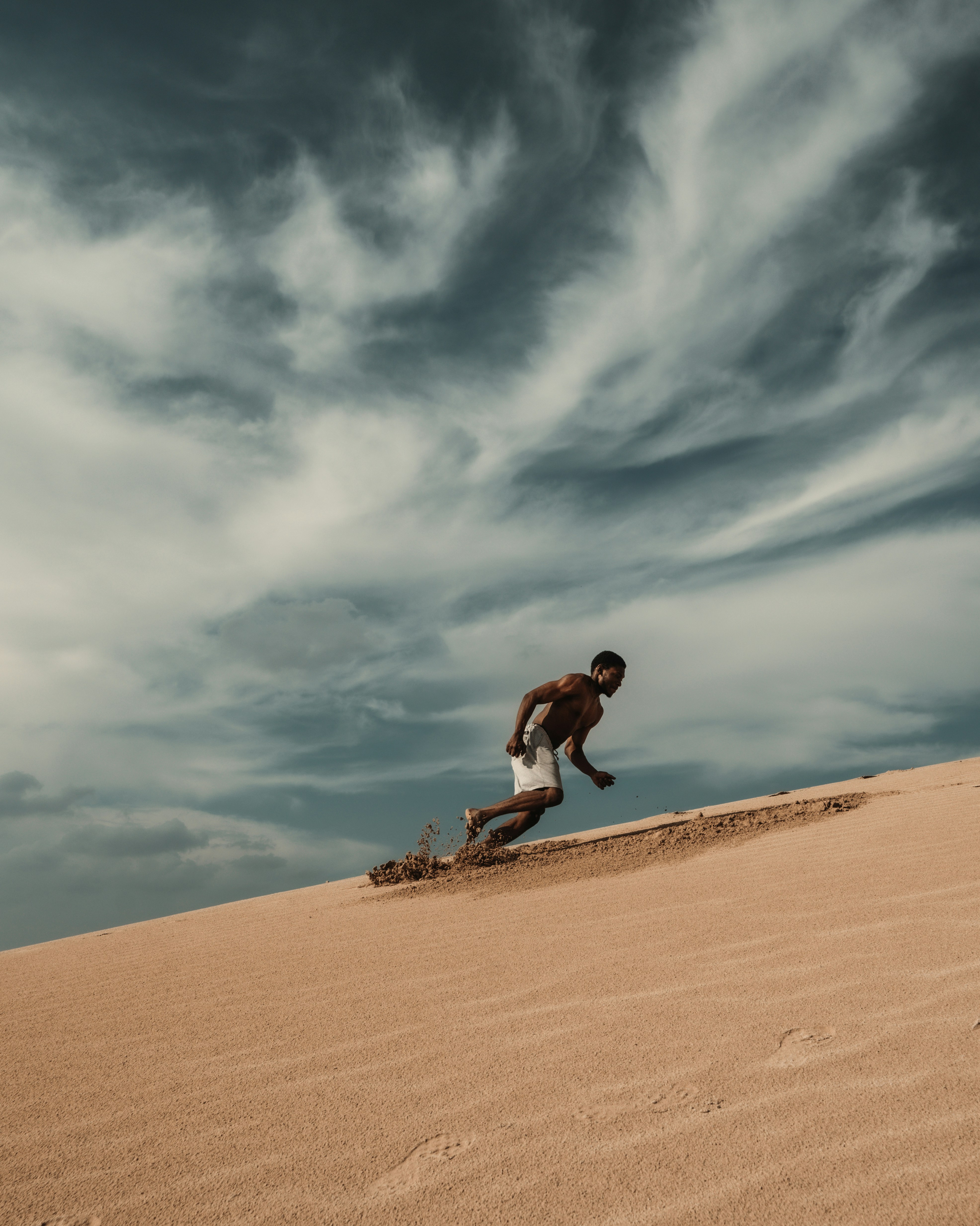 A man running down a steep sand dune under a dramatic cloudy sky