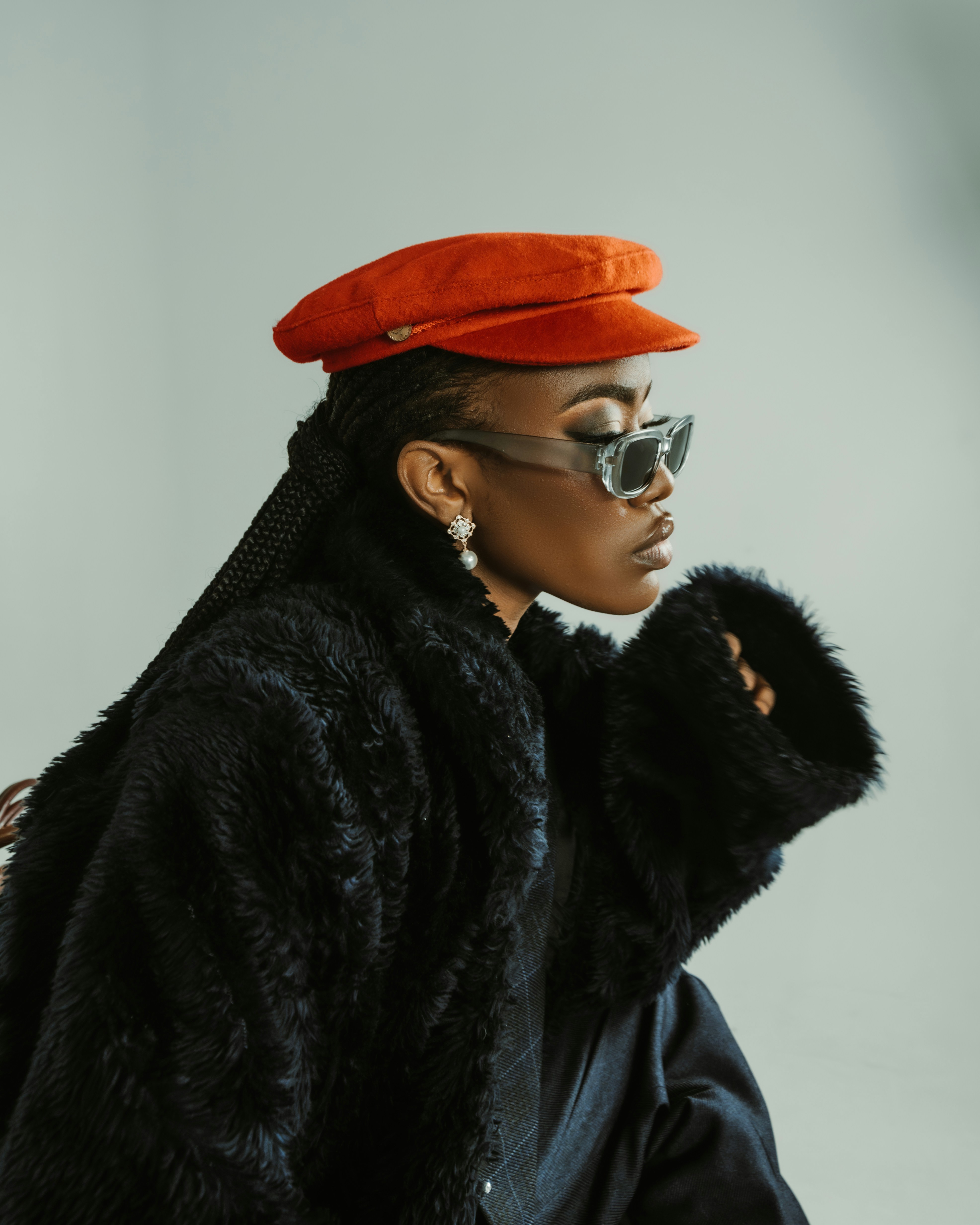 A person wearing a red cap, sunglasses, and a black faux fur coat