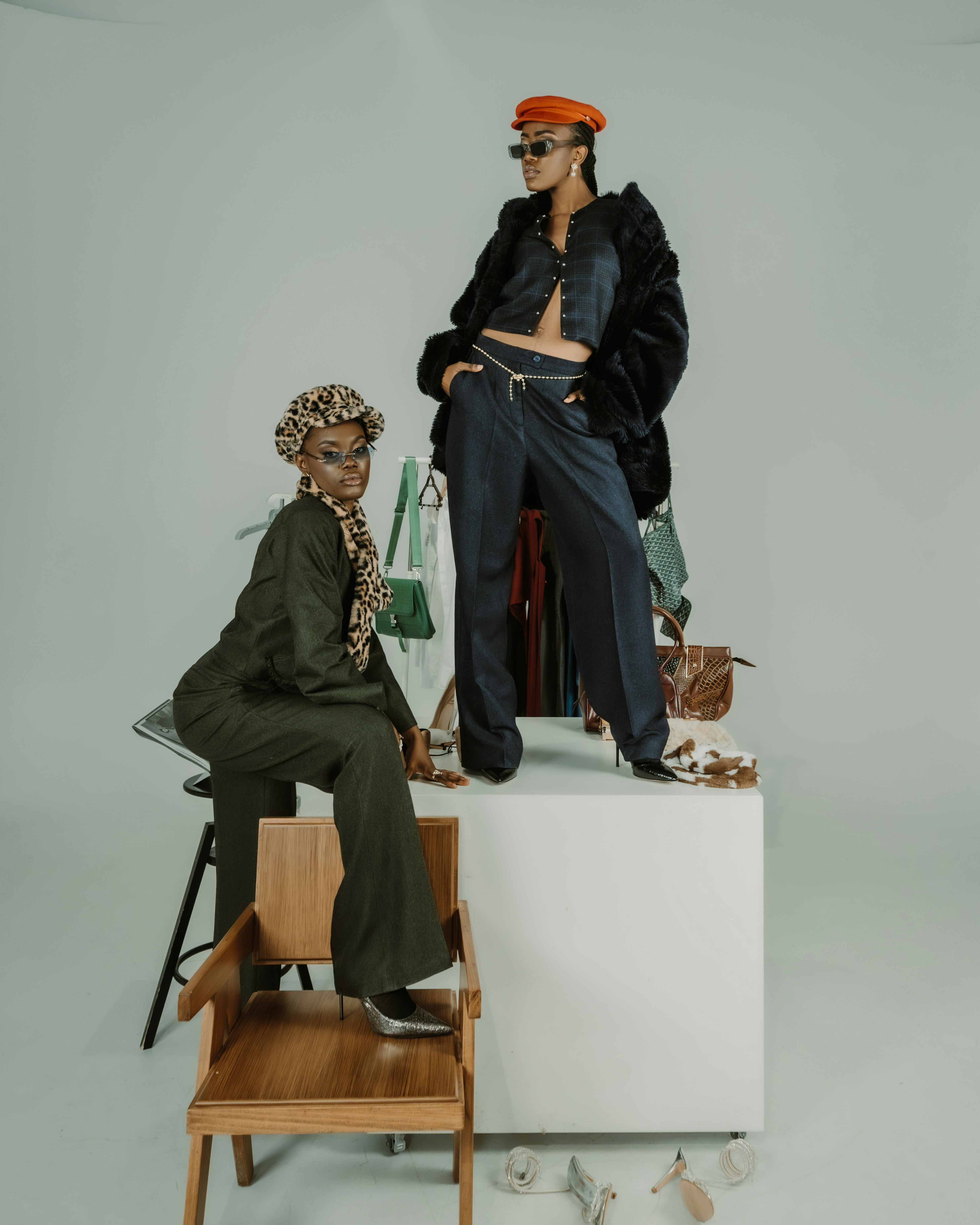 Two adults in stylish outfits posing on and beside a white pedestal in a studio