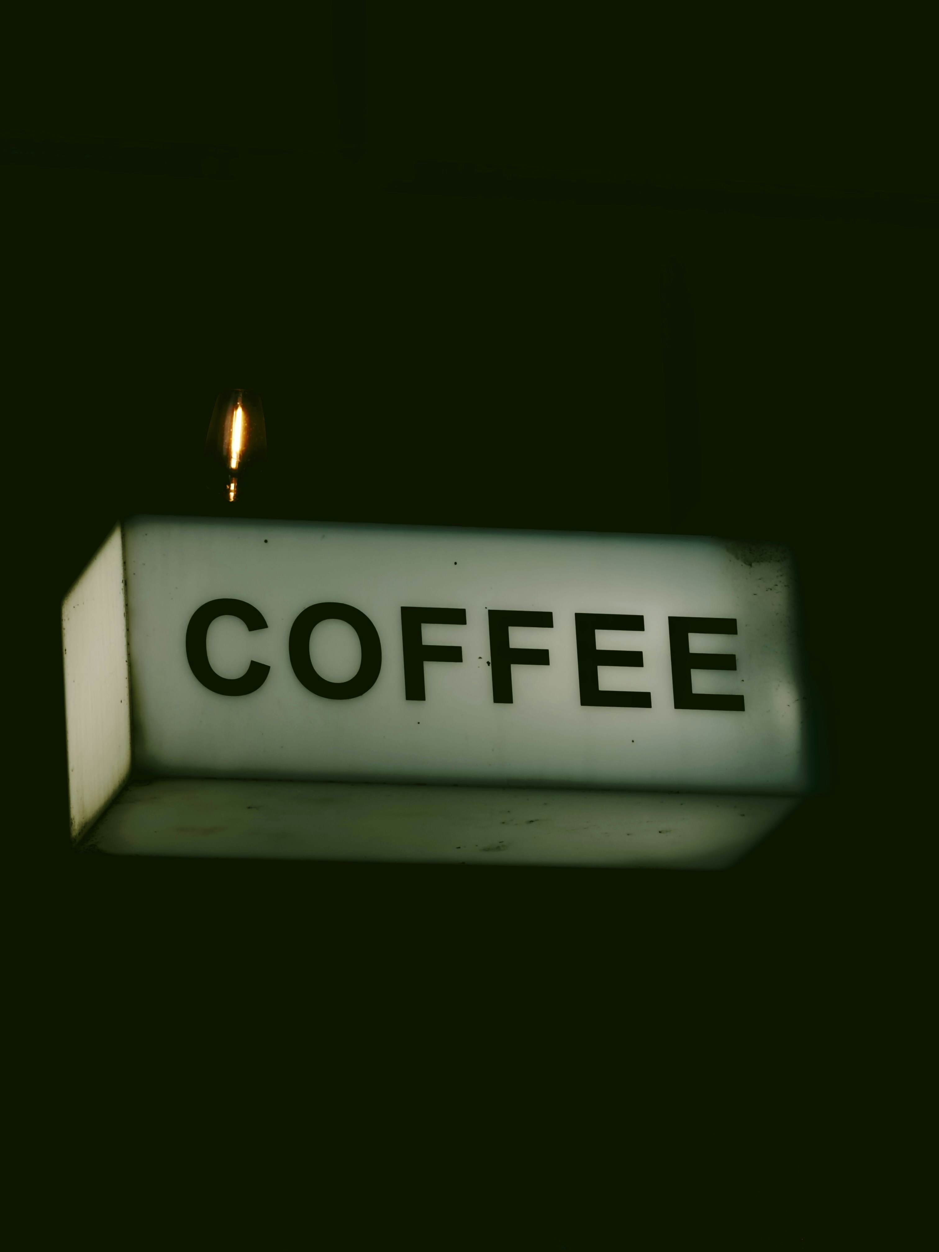 A glowing rectangular sign reading COFFEE with a small light bulb above it in the dark