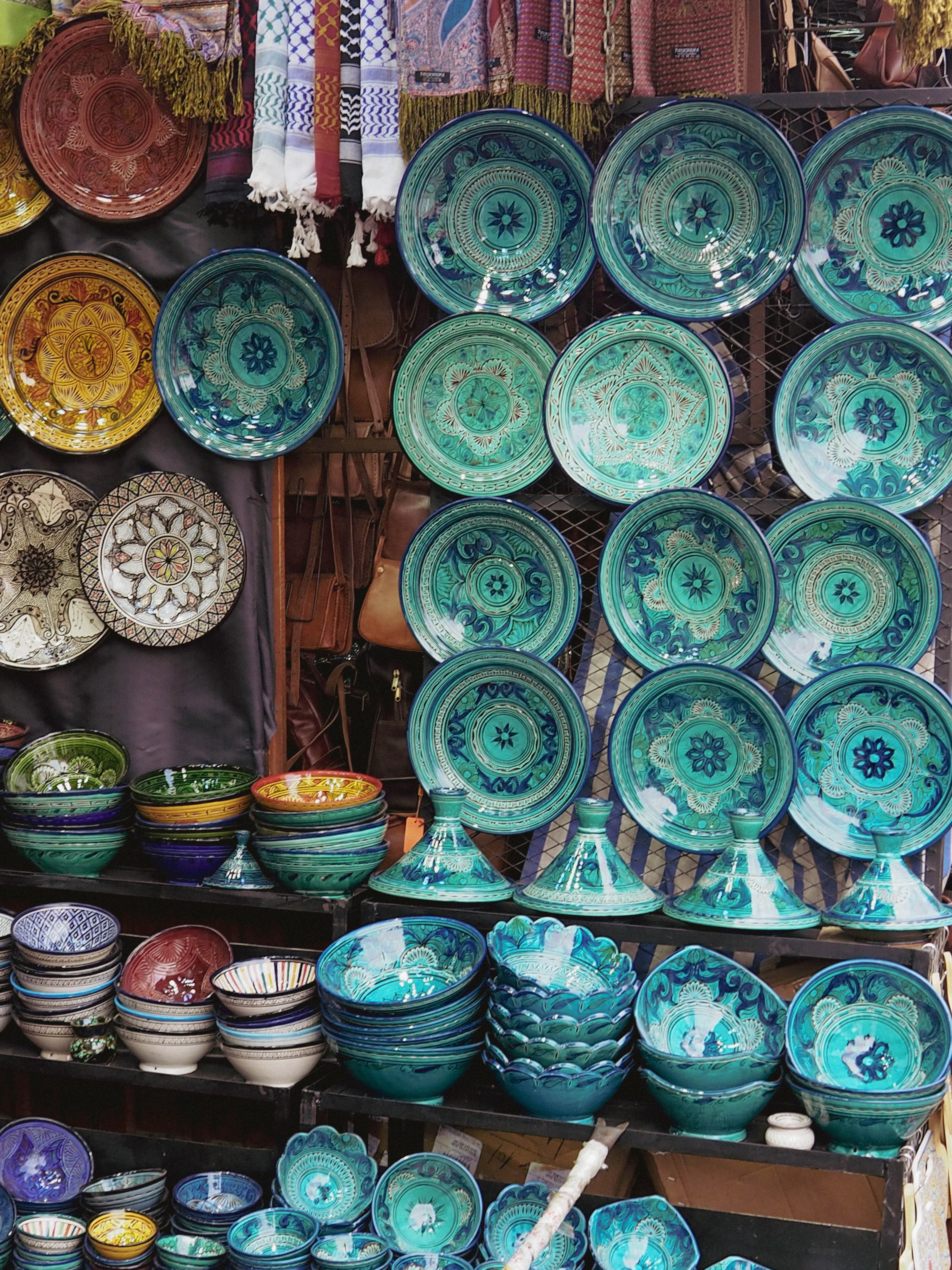 Handmade ceramic bowls, plates and tagines with blue and green patterns stacked on the shelves of a souk stall