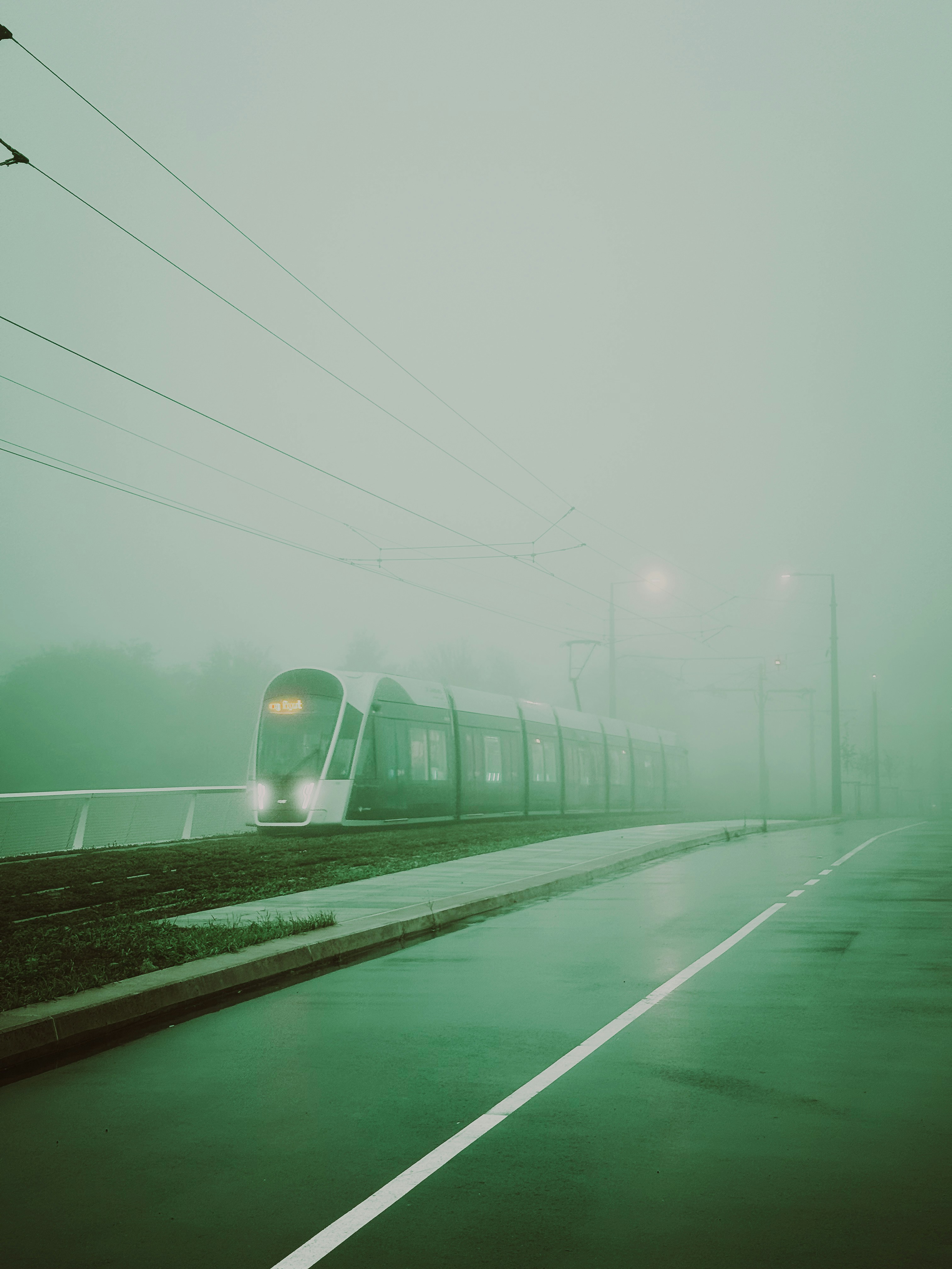 A modern tram moving along tracks on a foggy day with wet pavement
