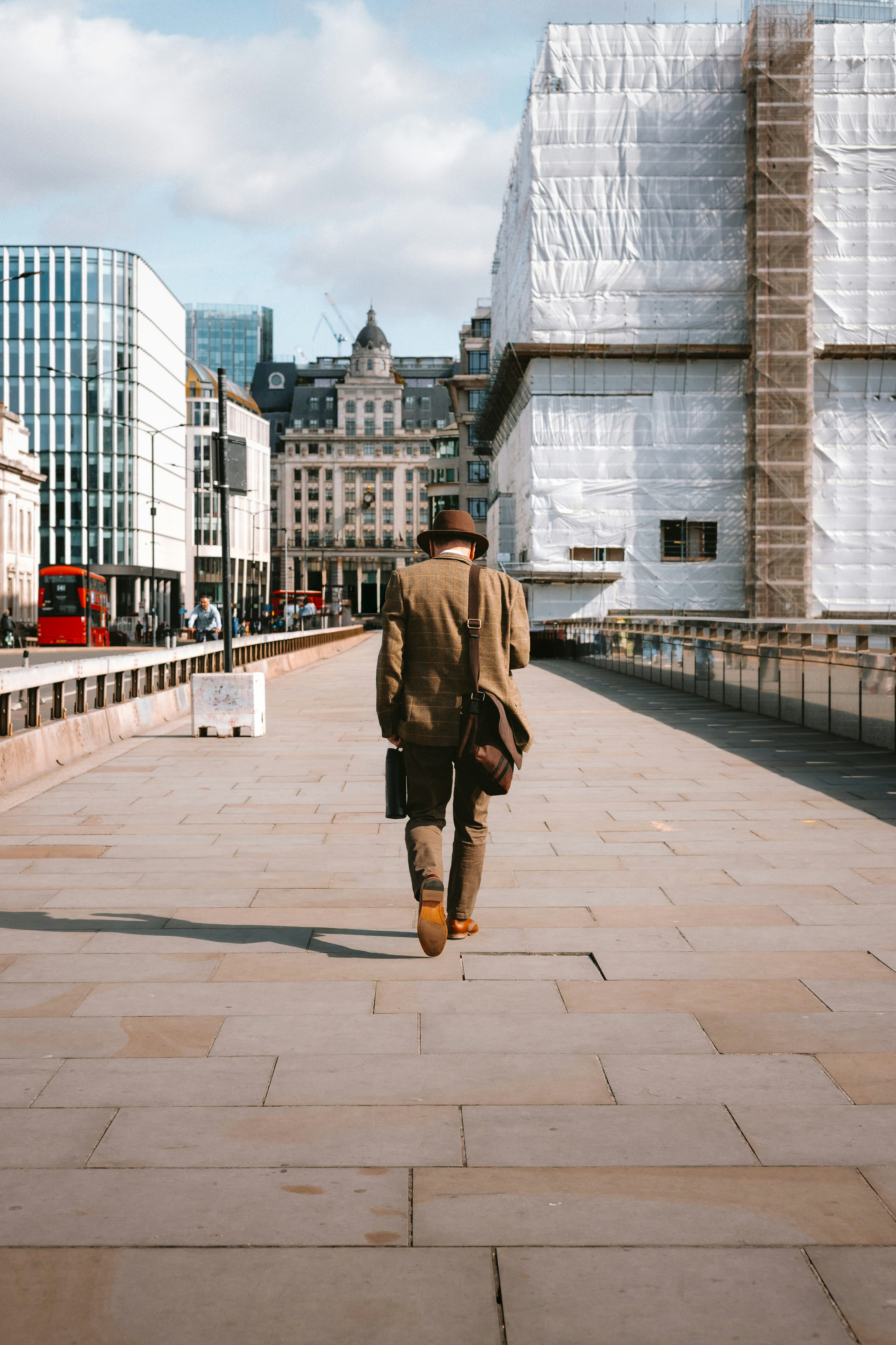 A person in a tweed jacket and hat walking across London Bridge in London