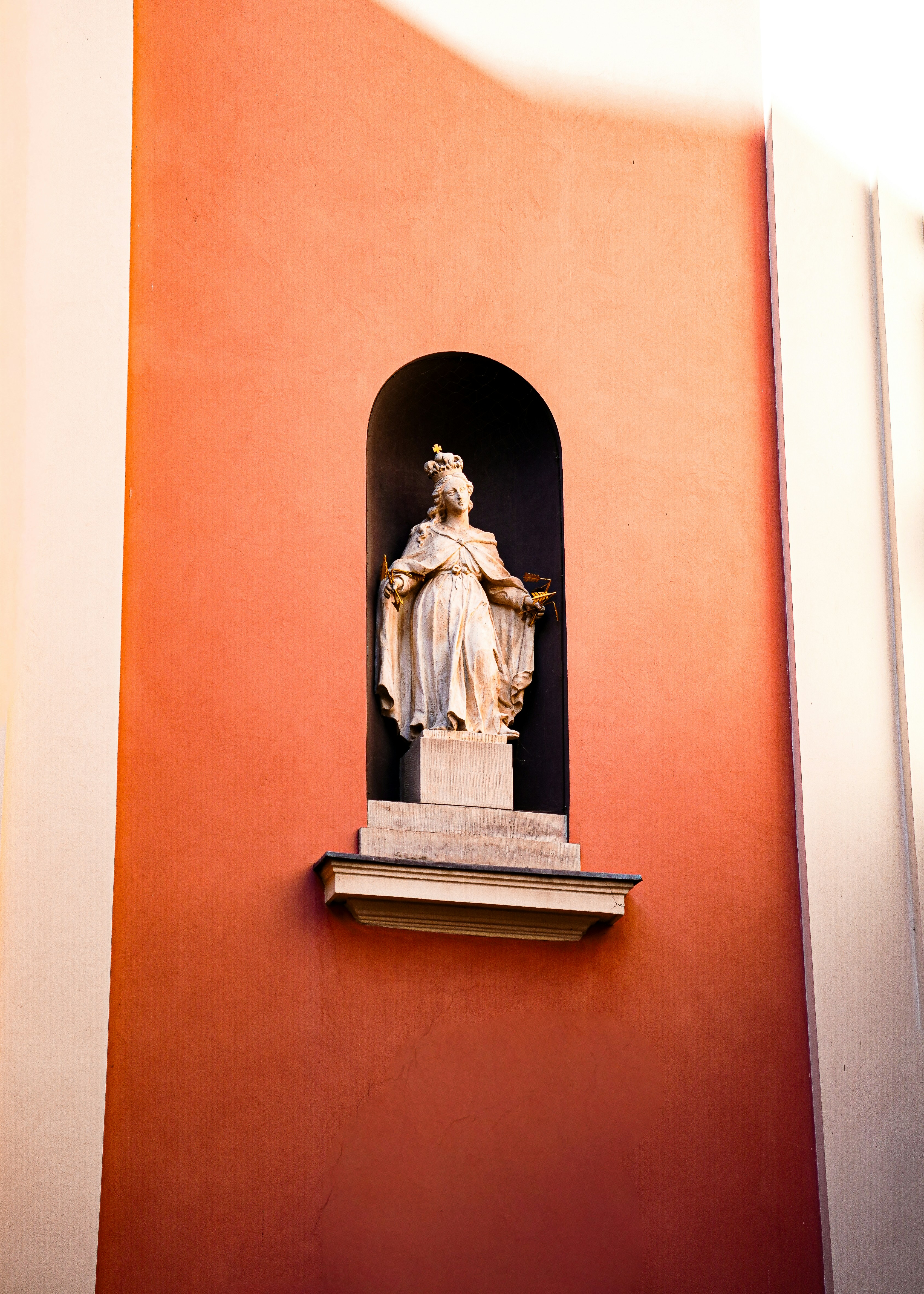 A stone statue of a crowned woman in a niche on an orange wall
