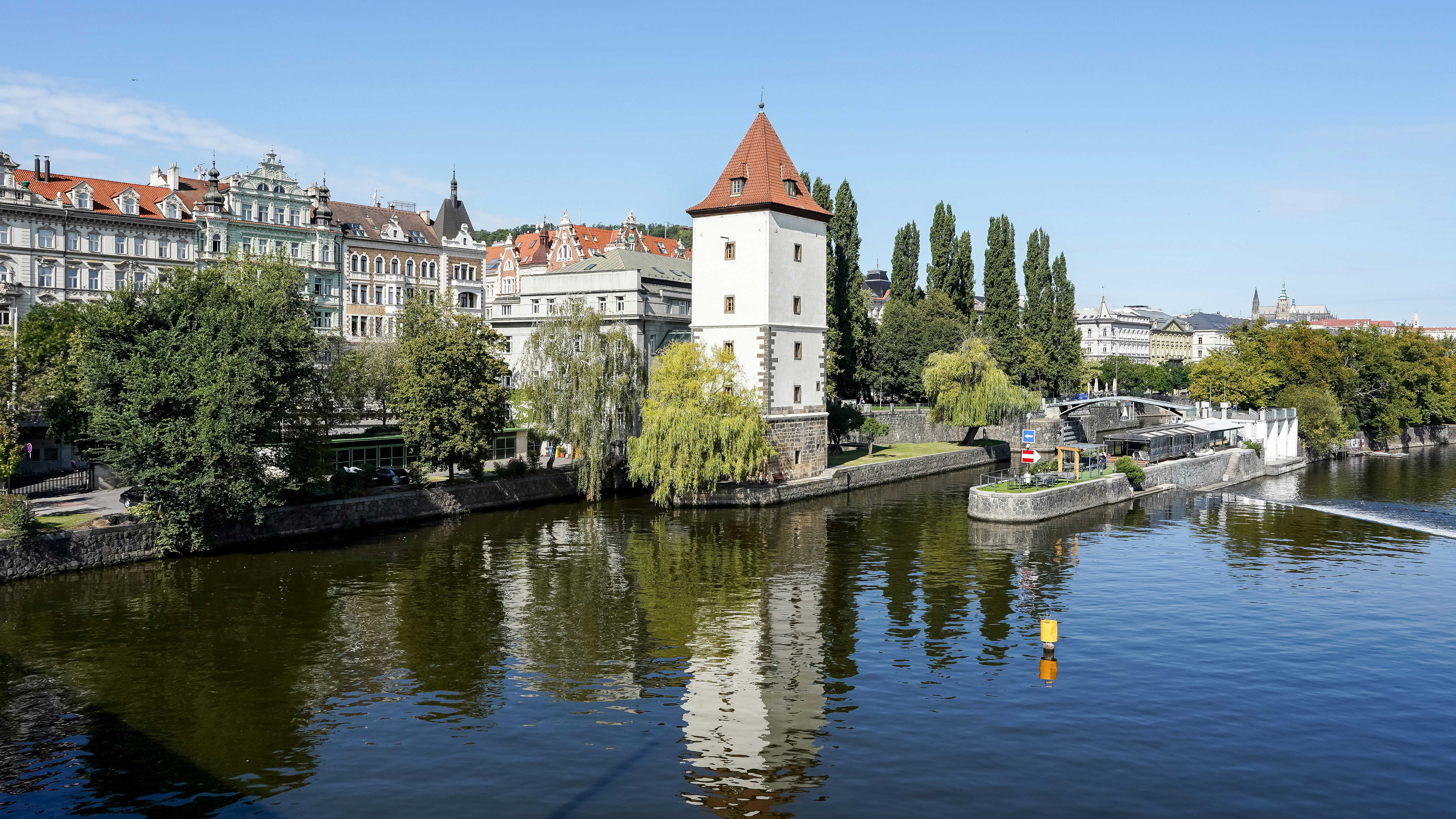 The Šítkovská water tower on the Vltava riverbank in Prague with historic buildings and trees