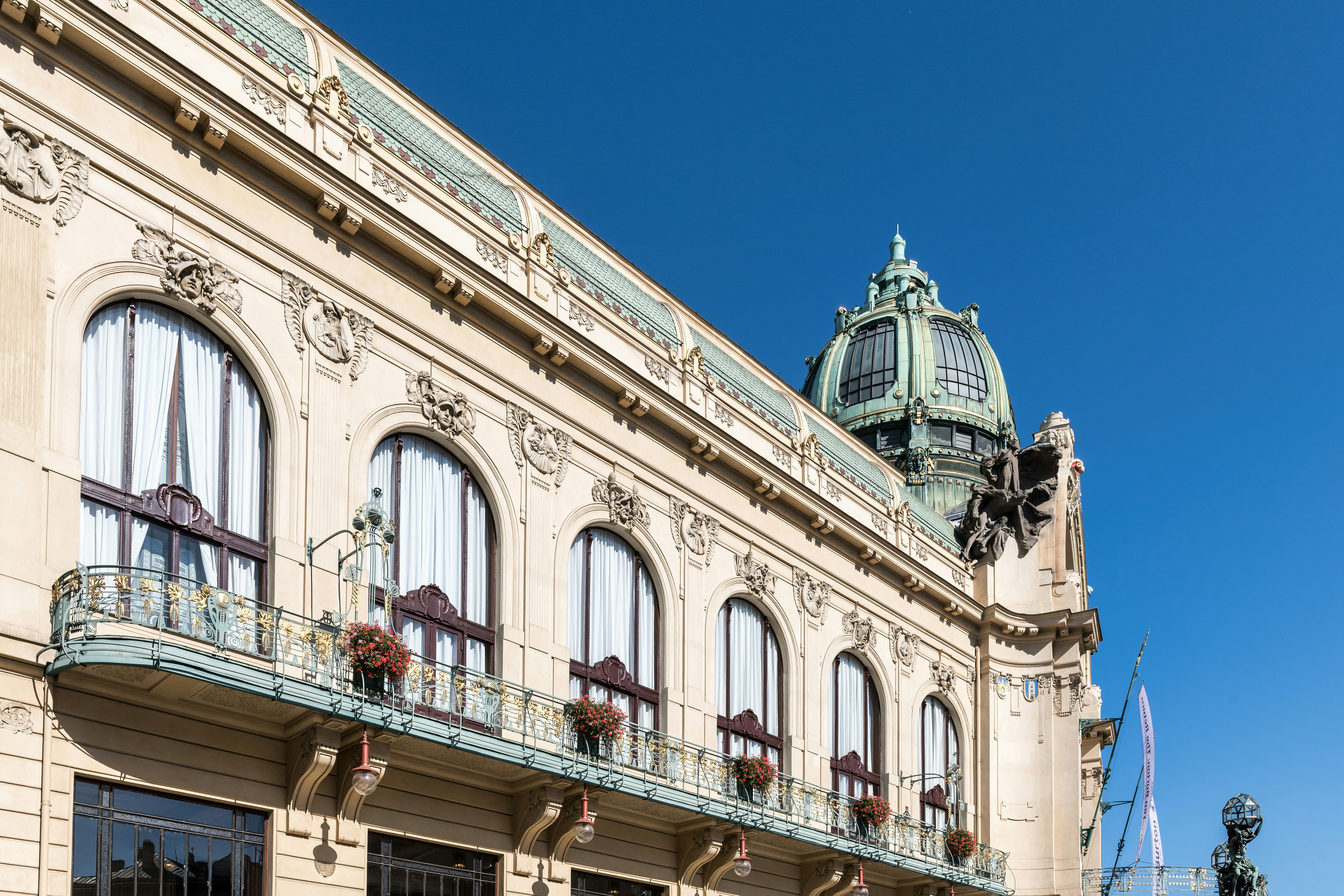 The ornate facade of the Municipal House in Prague with arched windows and a green dome