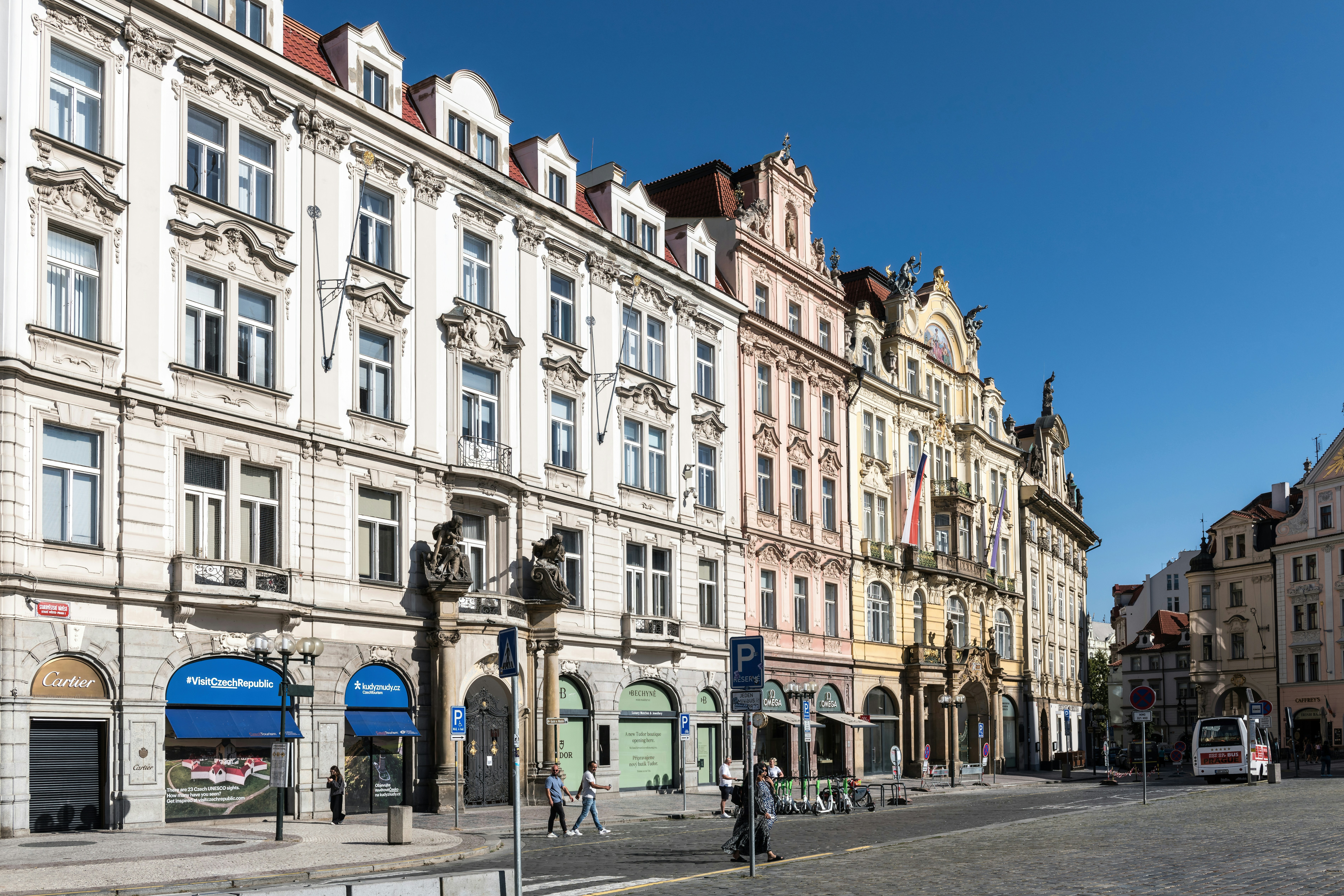 Ornate historic buildings along a cobblestone street in Prague under a clear blue sky