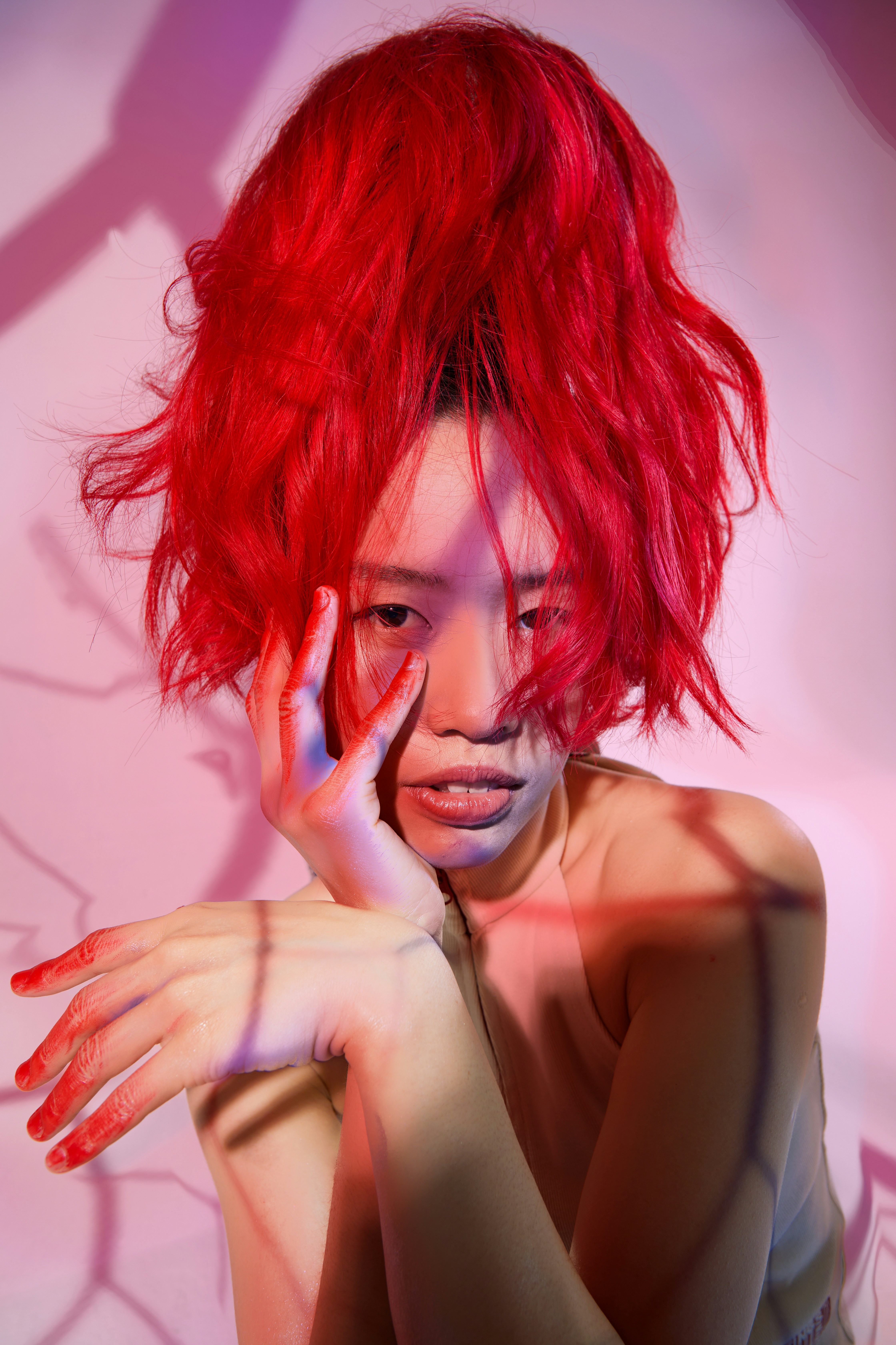 A person with vibrant red hair posing against a pink background with cast shadows