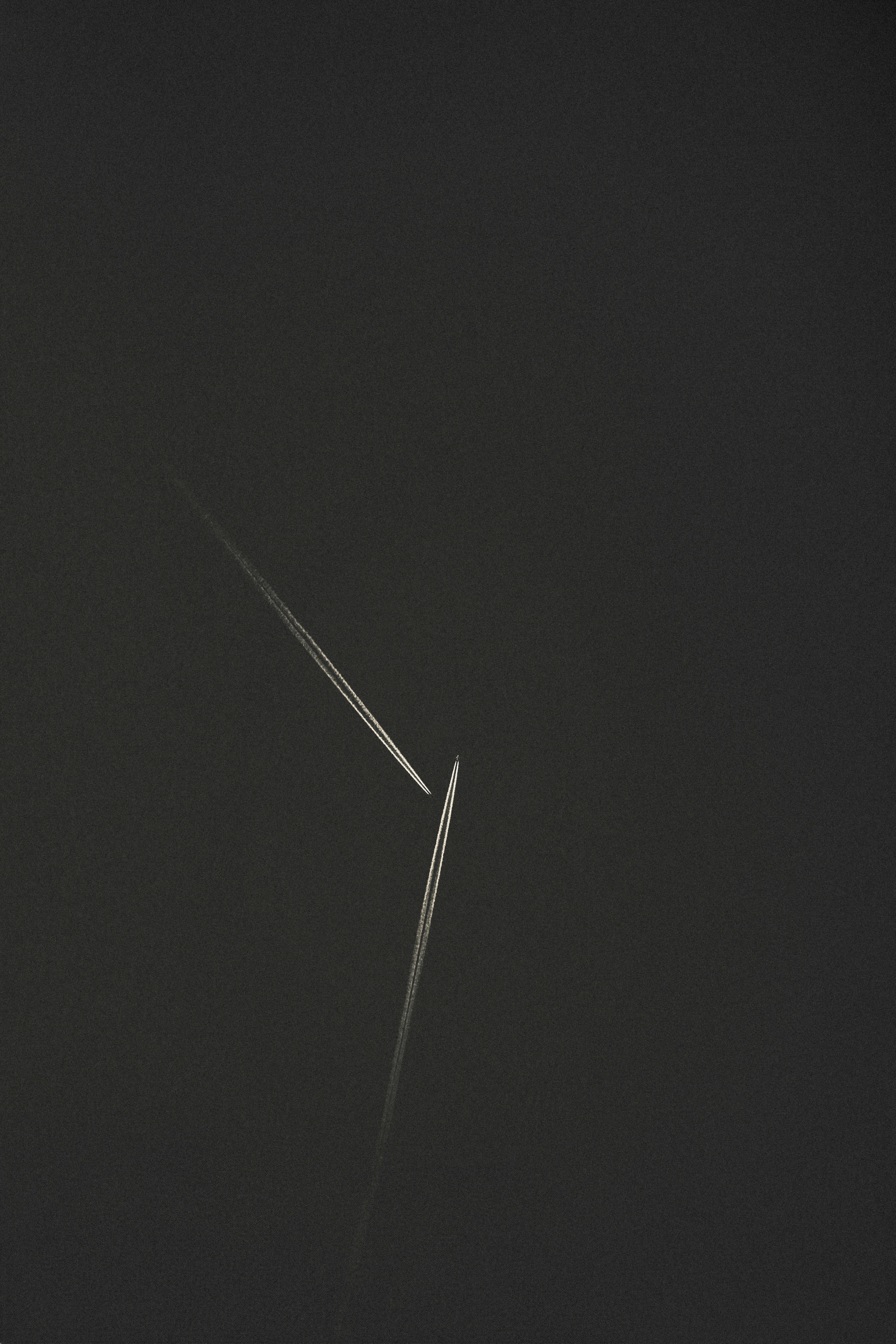 Two airplanes leaving white contrails crossing against a dark grey sky