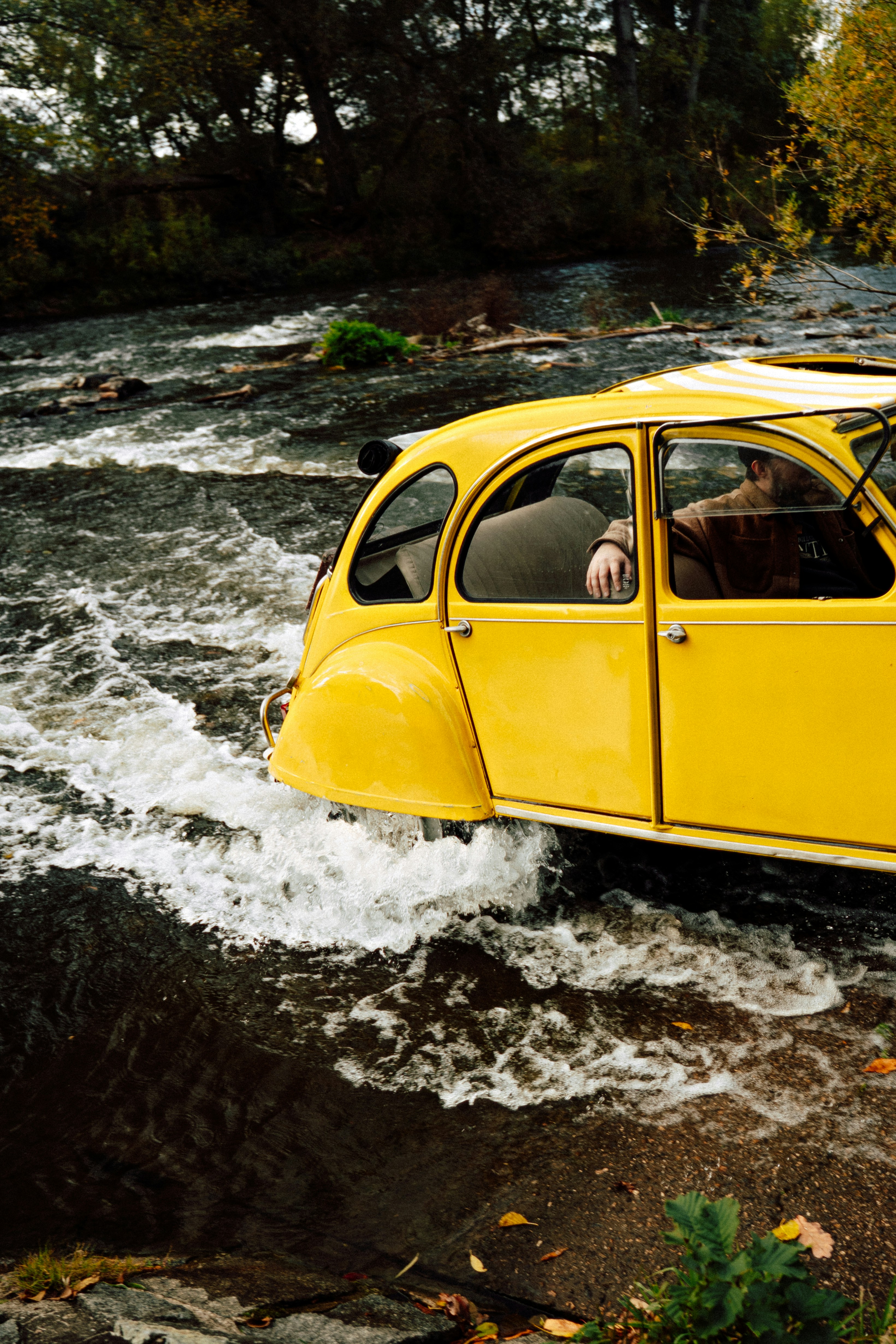 A bright yellow Citroen 2CV driving through a shallow river with splashing water - 相关推荐