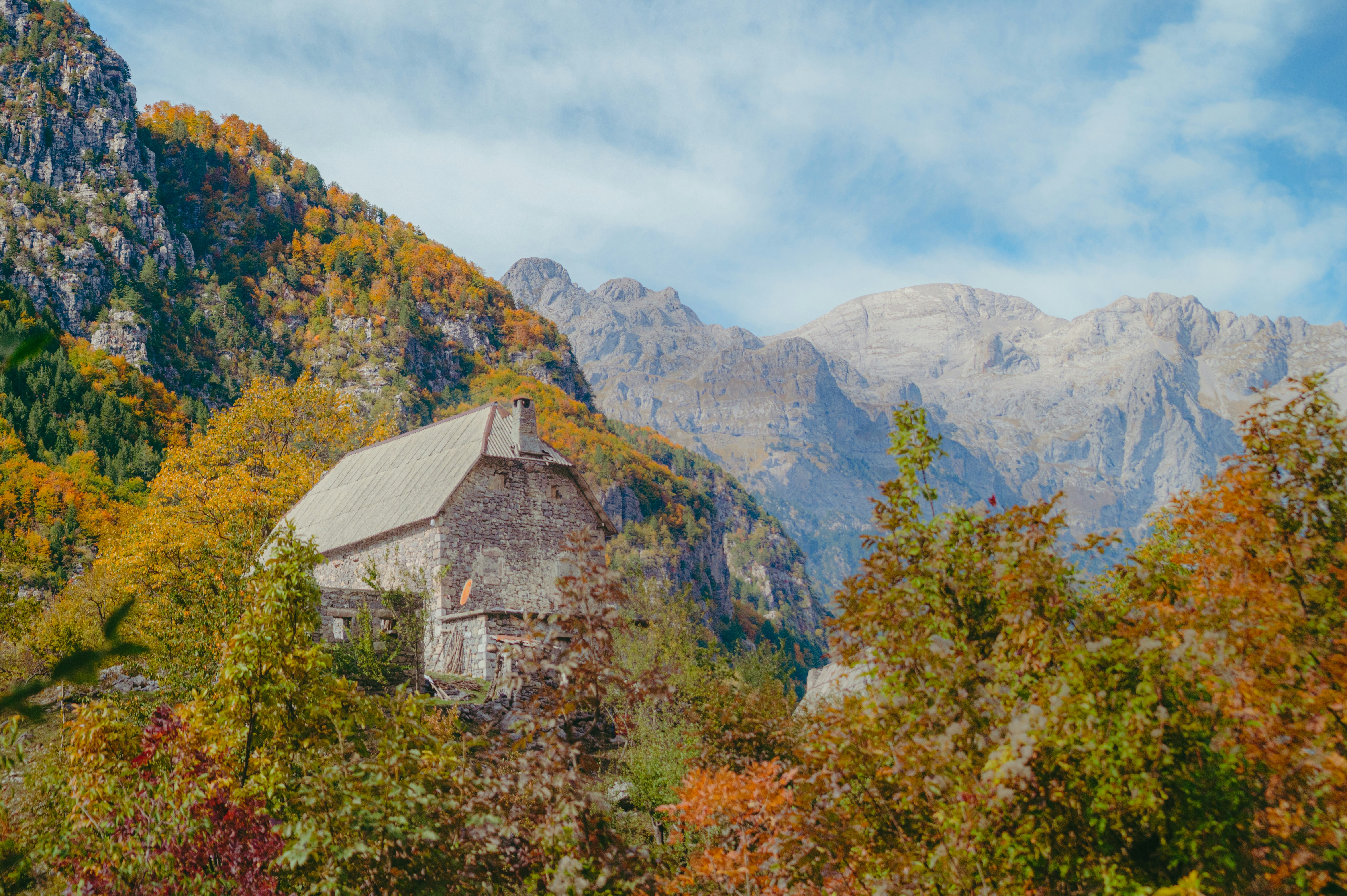 A stone house nestled in a valley with autumn foliage beneath towering rocky mountains