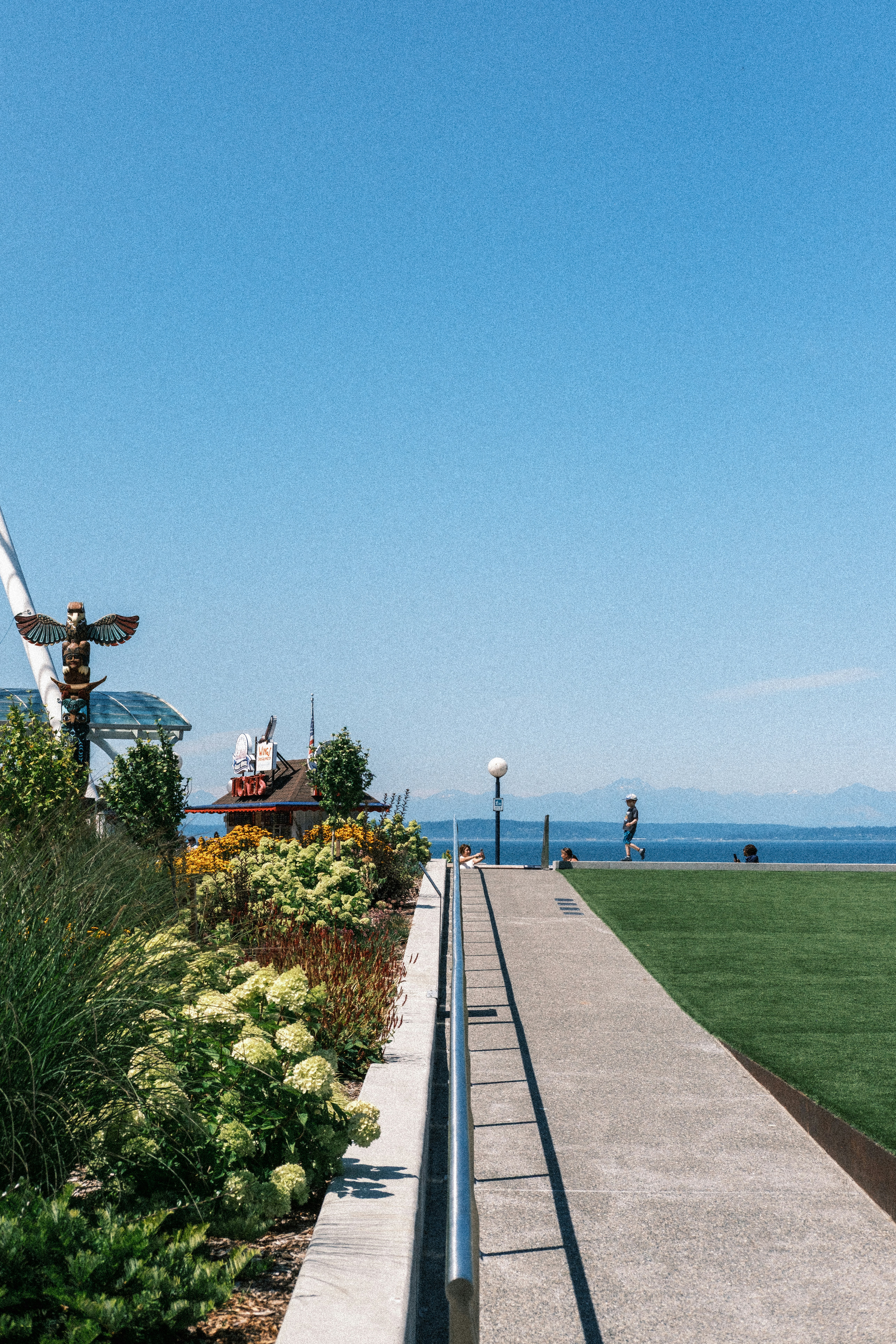 A totem pole beside a garden path overlooking the ocean and distant mountains