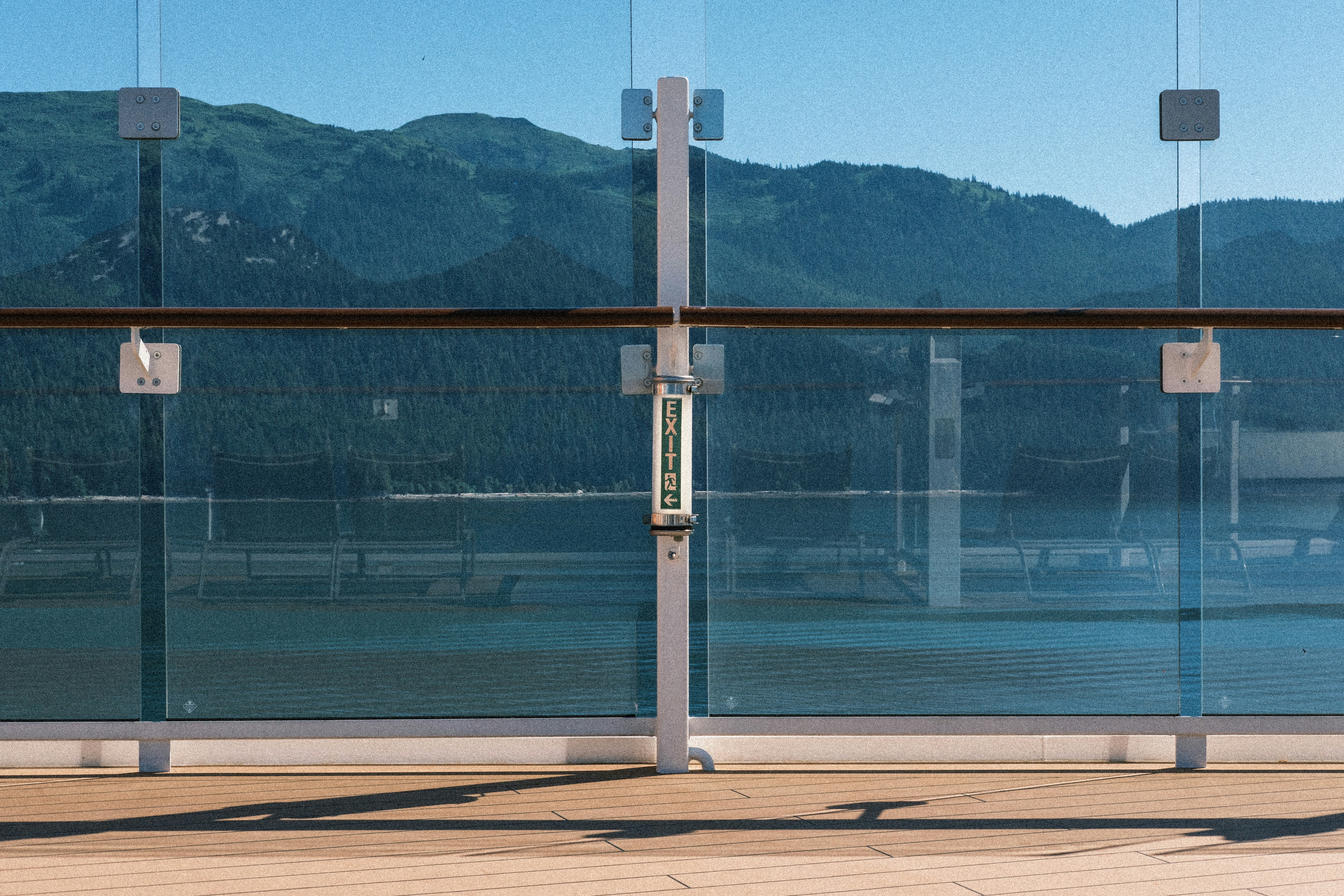 A glass railing with a wooden handrail and an exit sign overlooking mountains