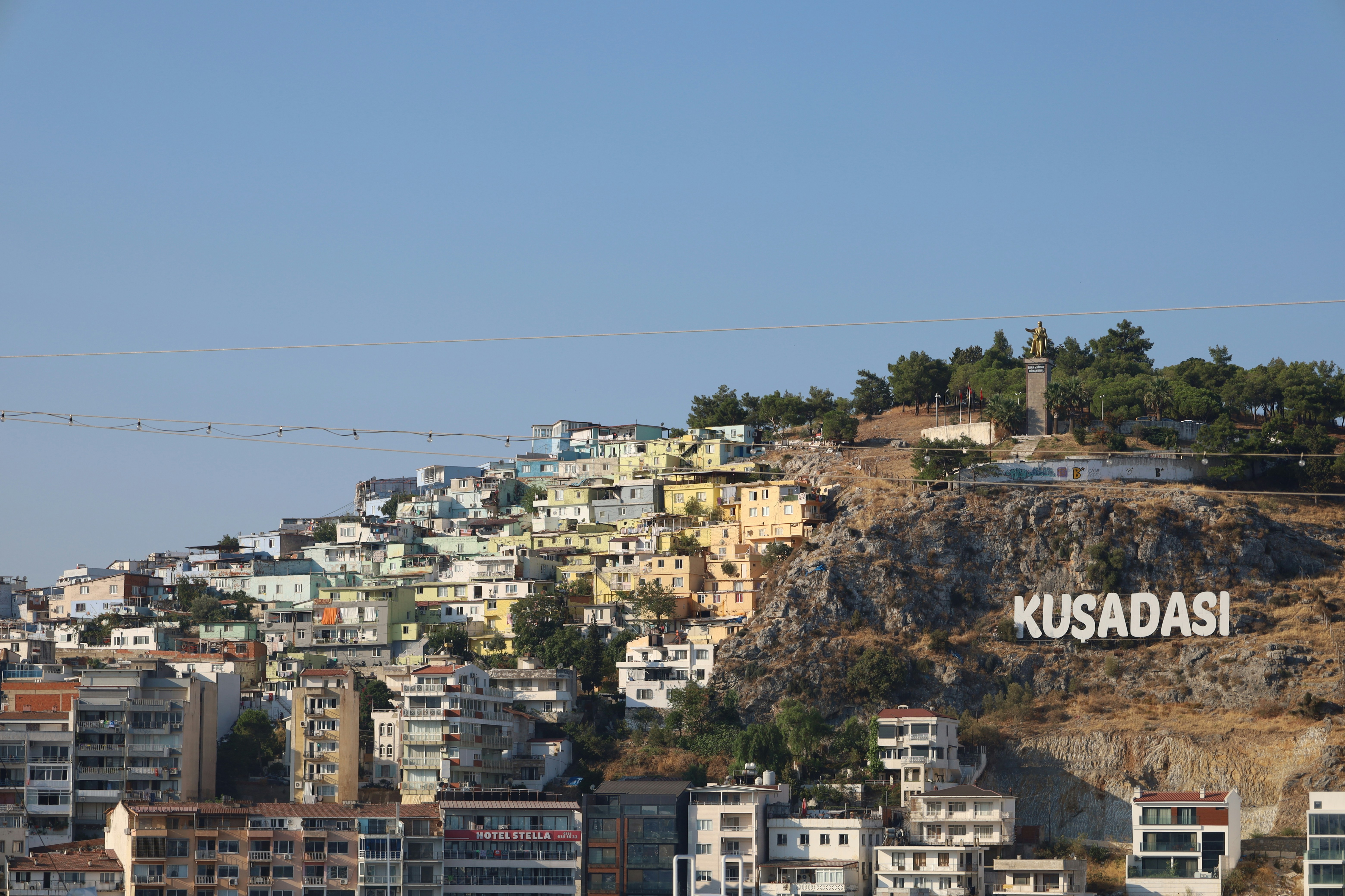 Fotomural The hillside town of Kusadasi with colorful houses and a large sign on the rocky slope