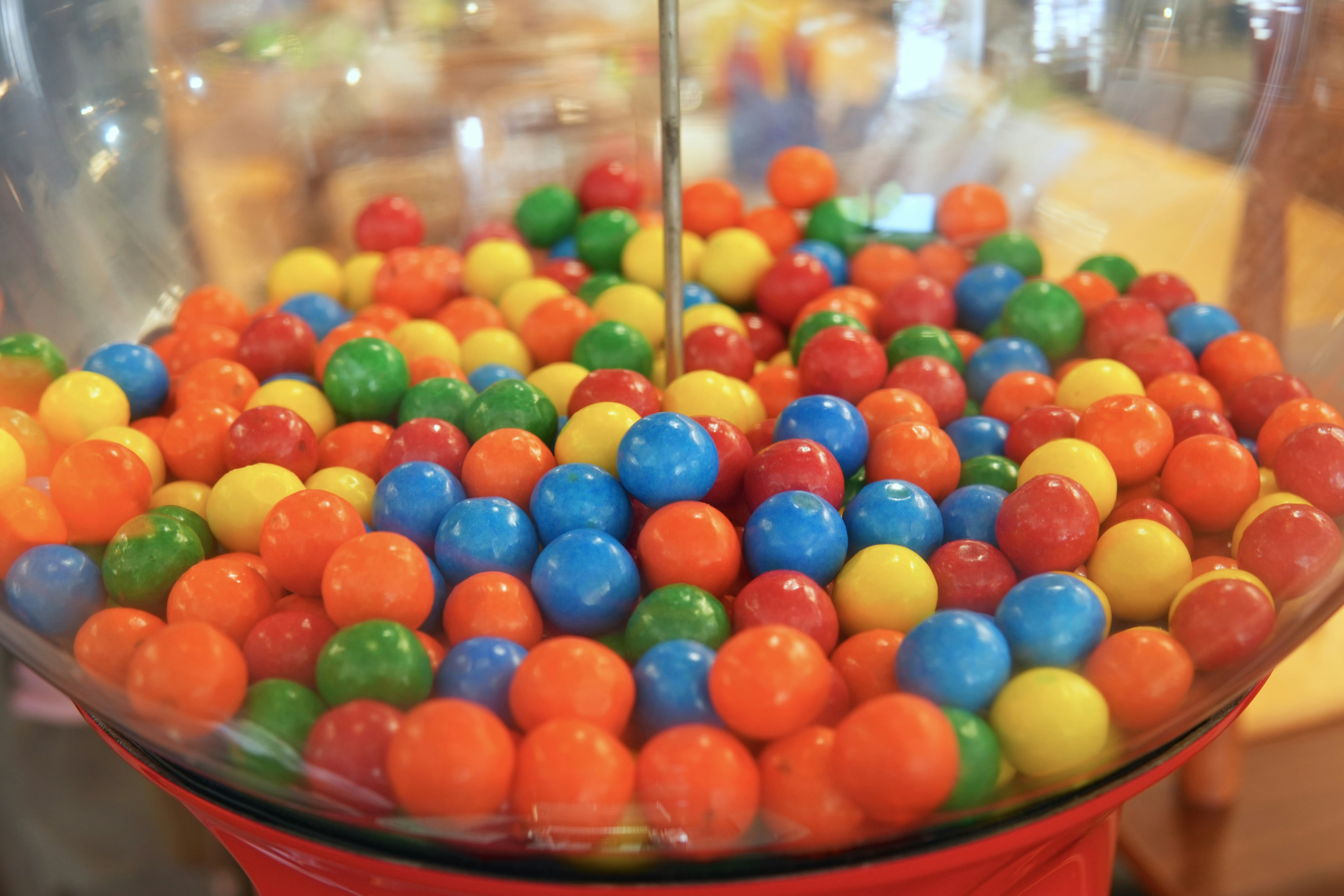 A clear glass gumball machine filled with colorful red, blue, yellow, and green gumballs