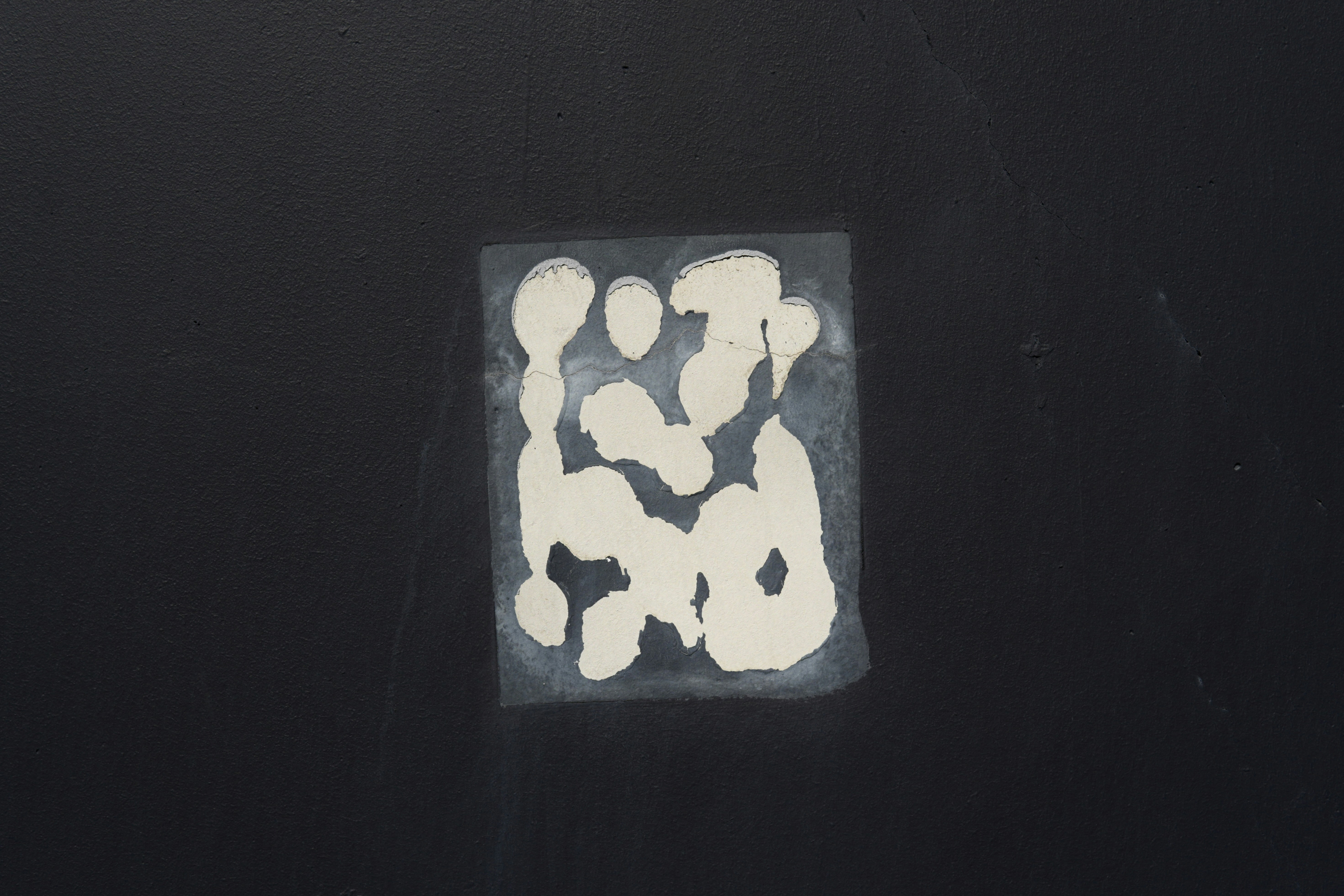 A rectangular patch of peeling cream paint revealing a dark grey surface on a black wall