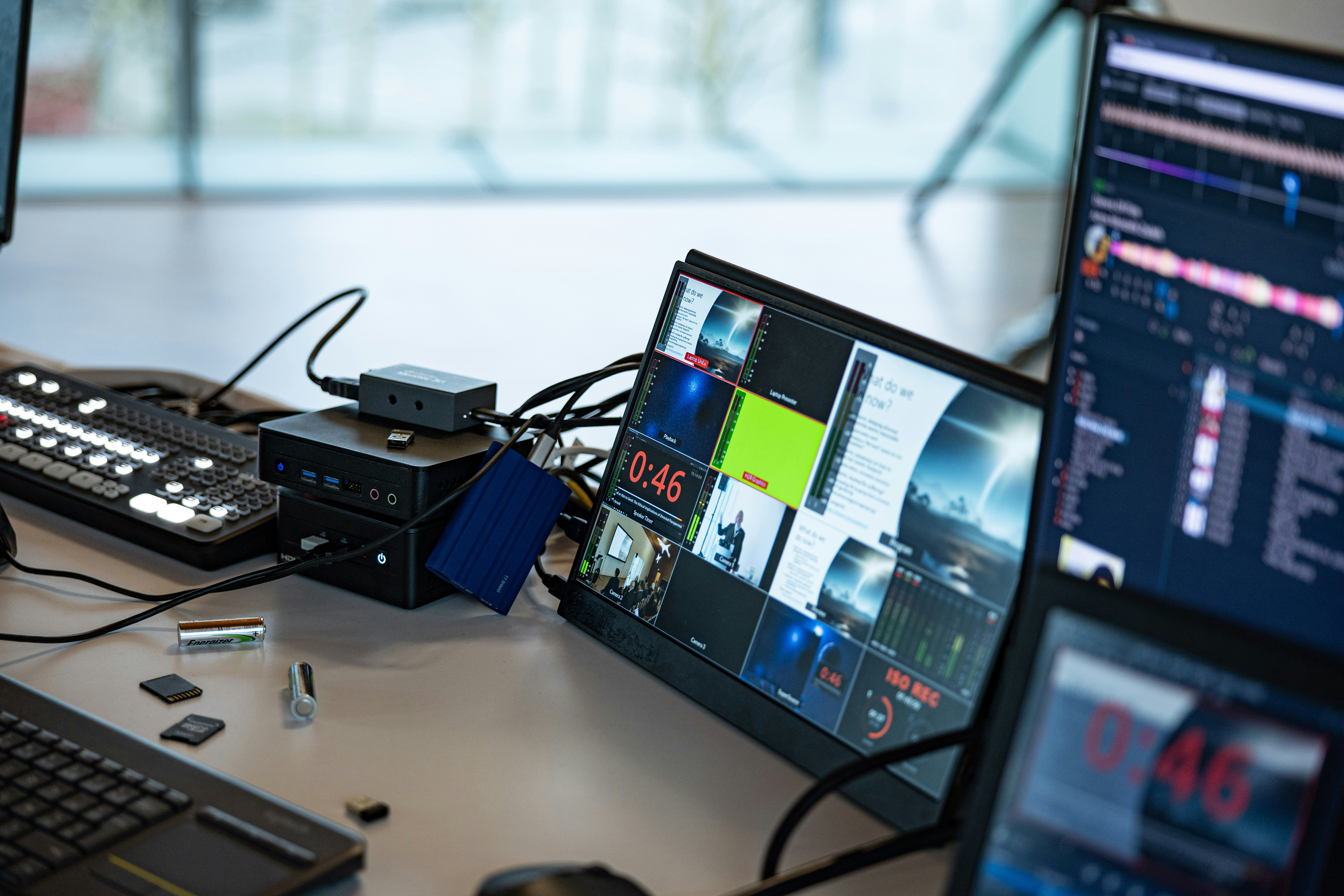 A video production workstation with multiple monitors displaying live feeds and audio levels on a desk