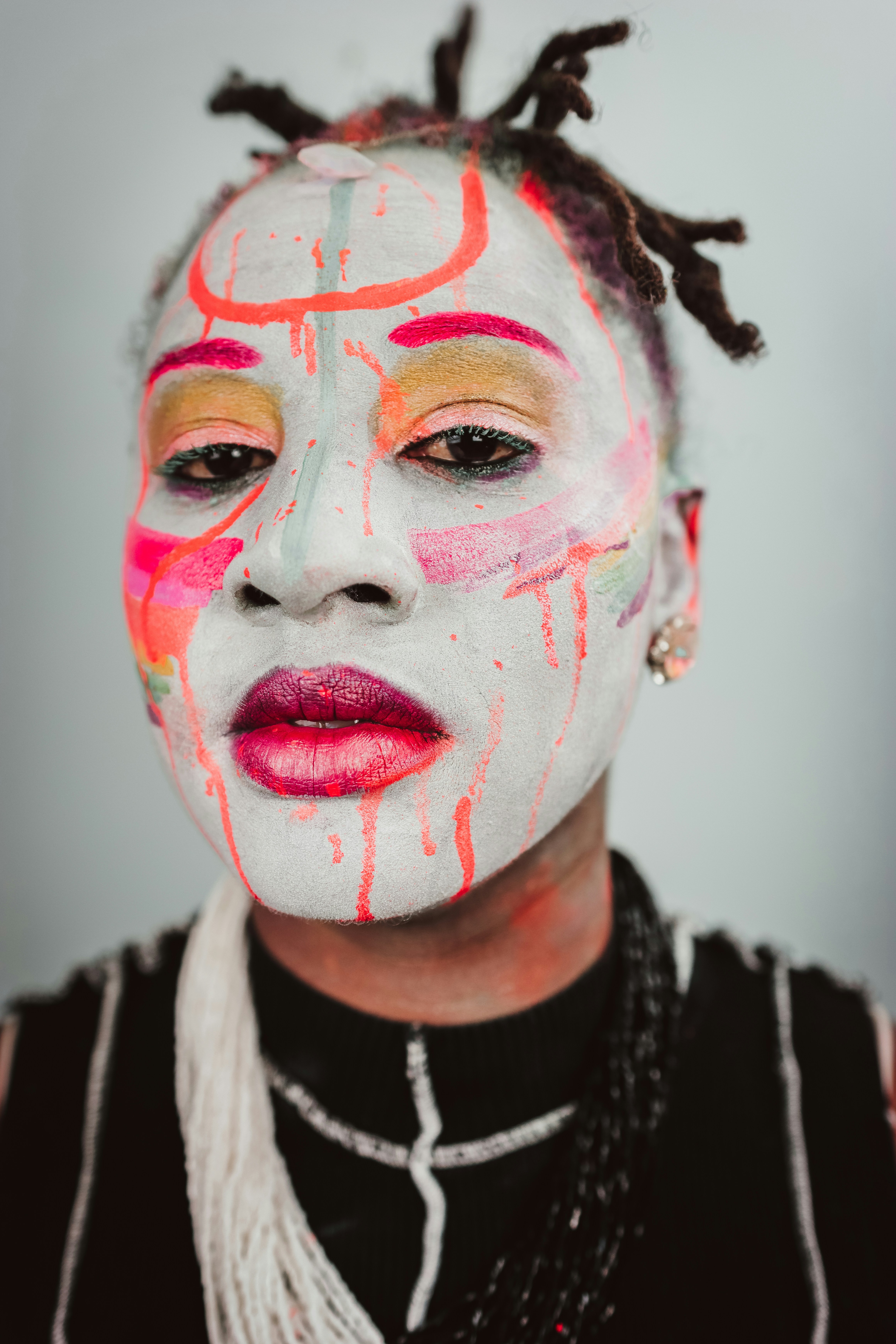 A person with white face paint and vibrant neon orange and pink abstract markings