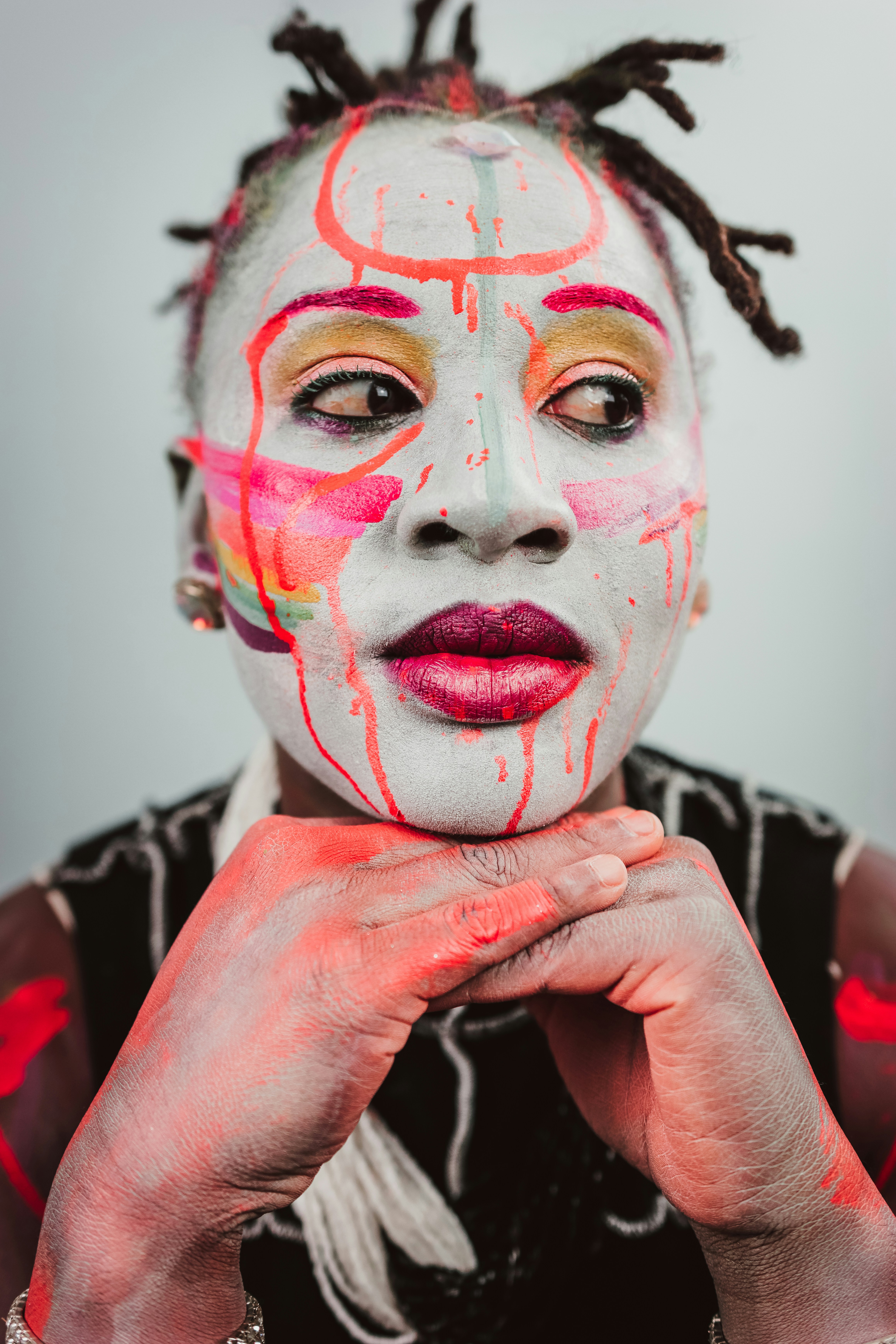 A person with white face paint and colorful abstract markings resting their chin on their hands