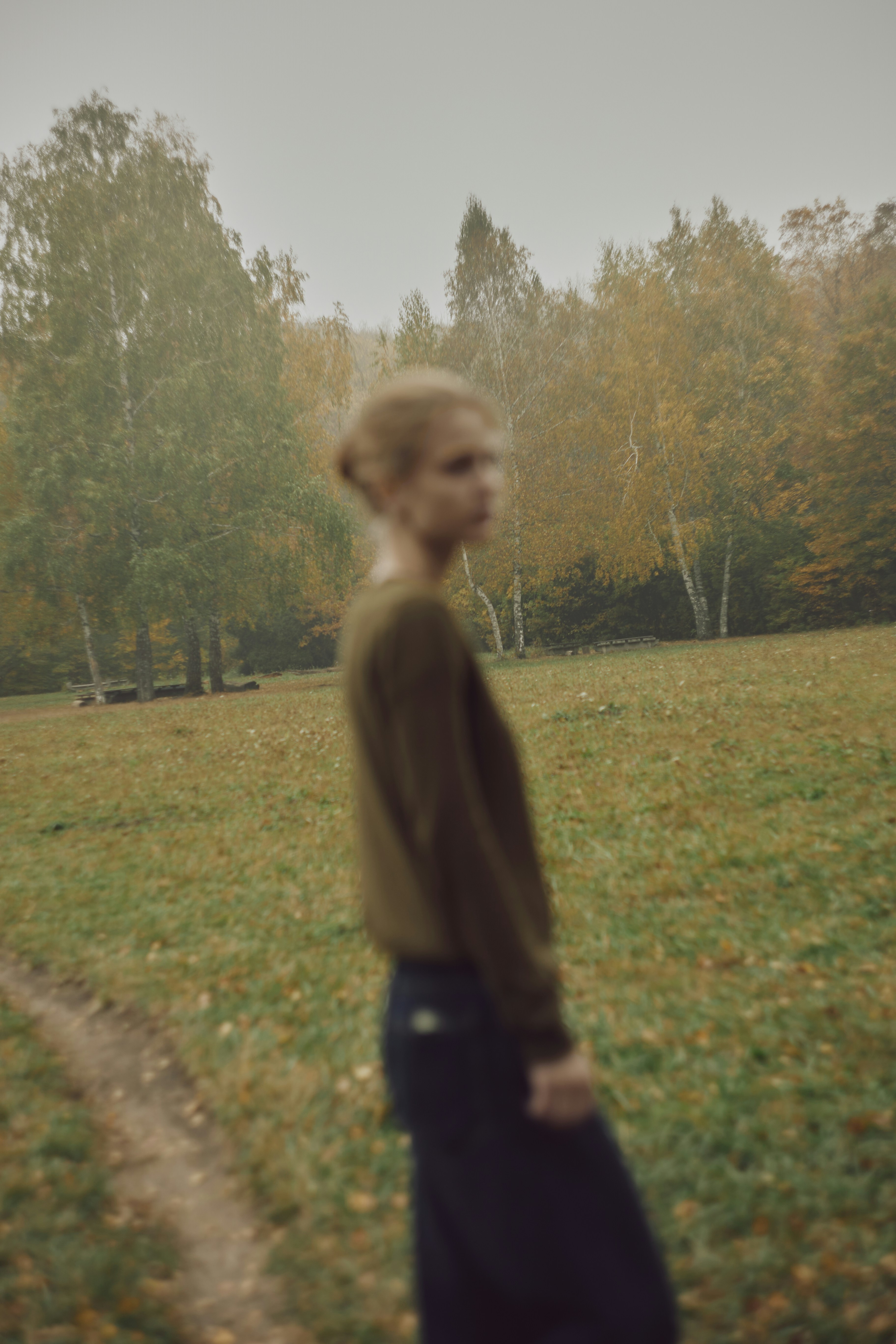 A person in a brown sweater standing in a misty autumn forest clearing