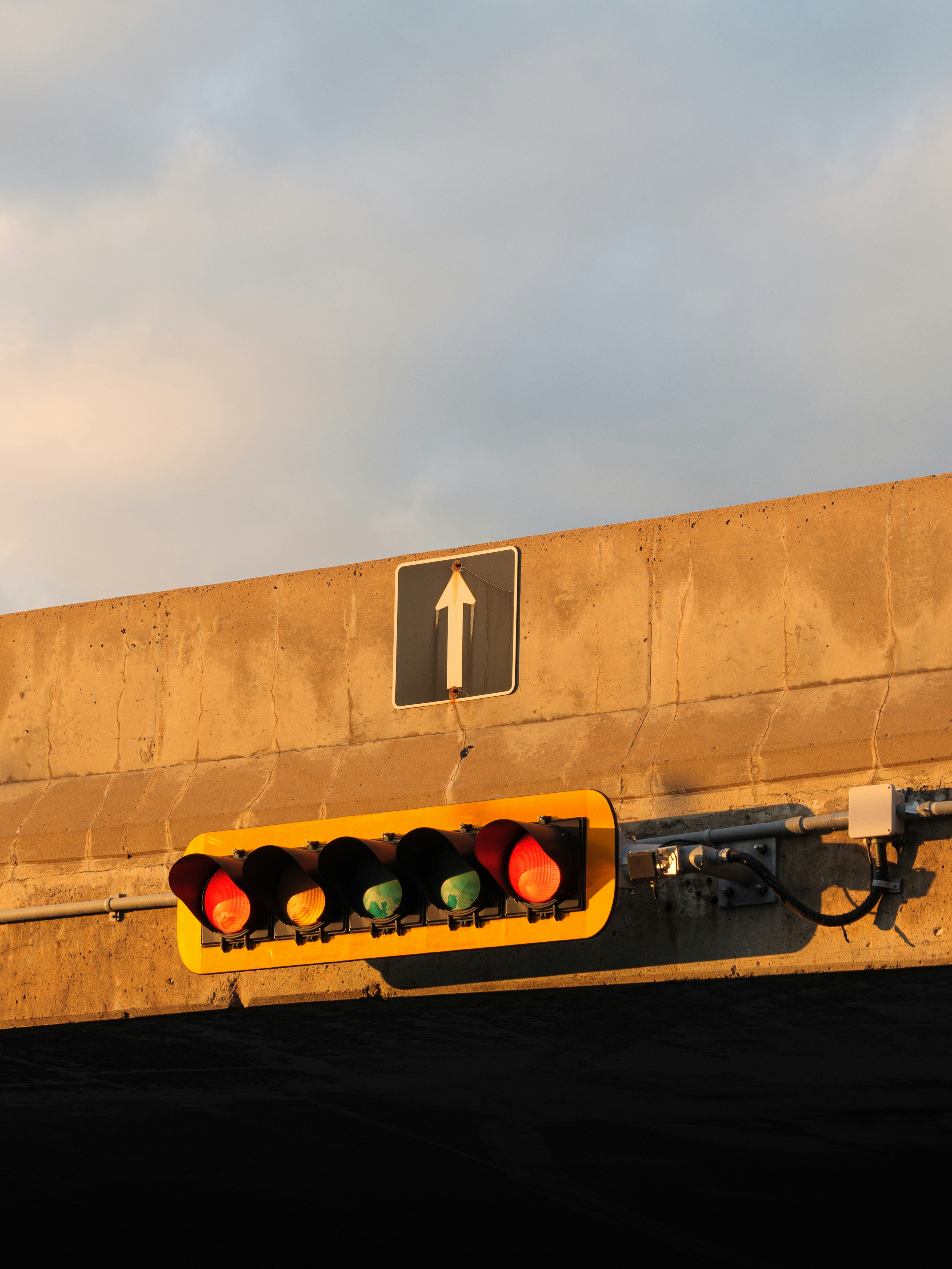 A horizontal traffic signal with red lights on a concrete overpass under a warm sky