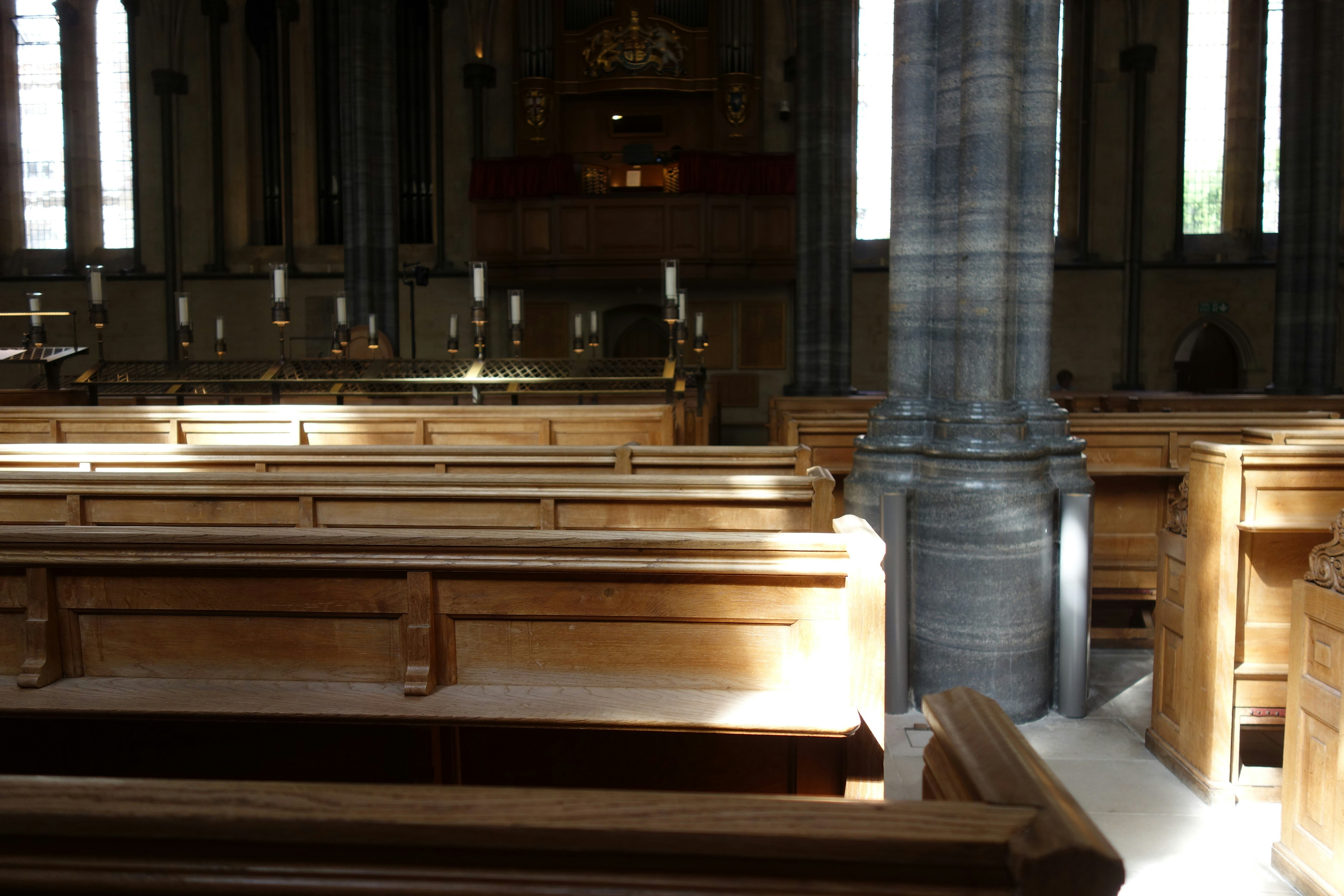 Wooden pews in a sunlit church interior with a large stone column