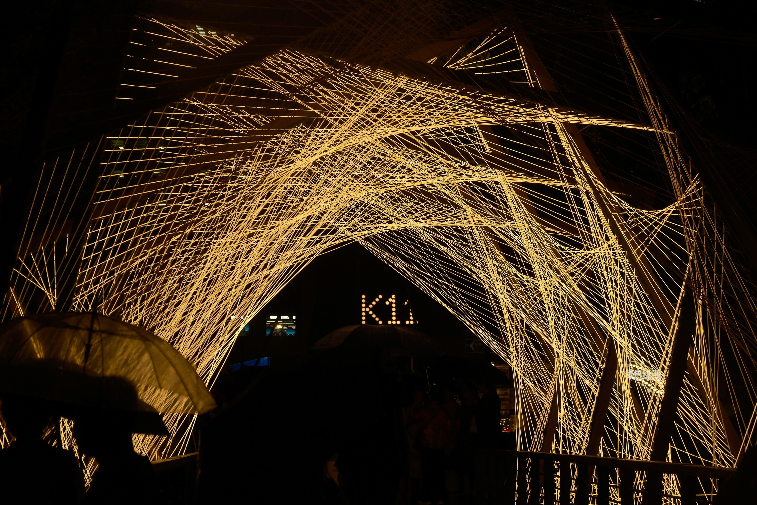 A glowing geometric string installation forming an archway over a dark street at night