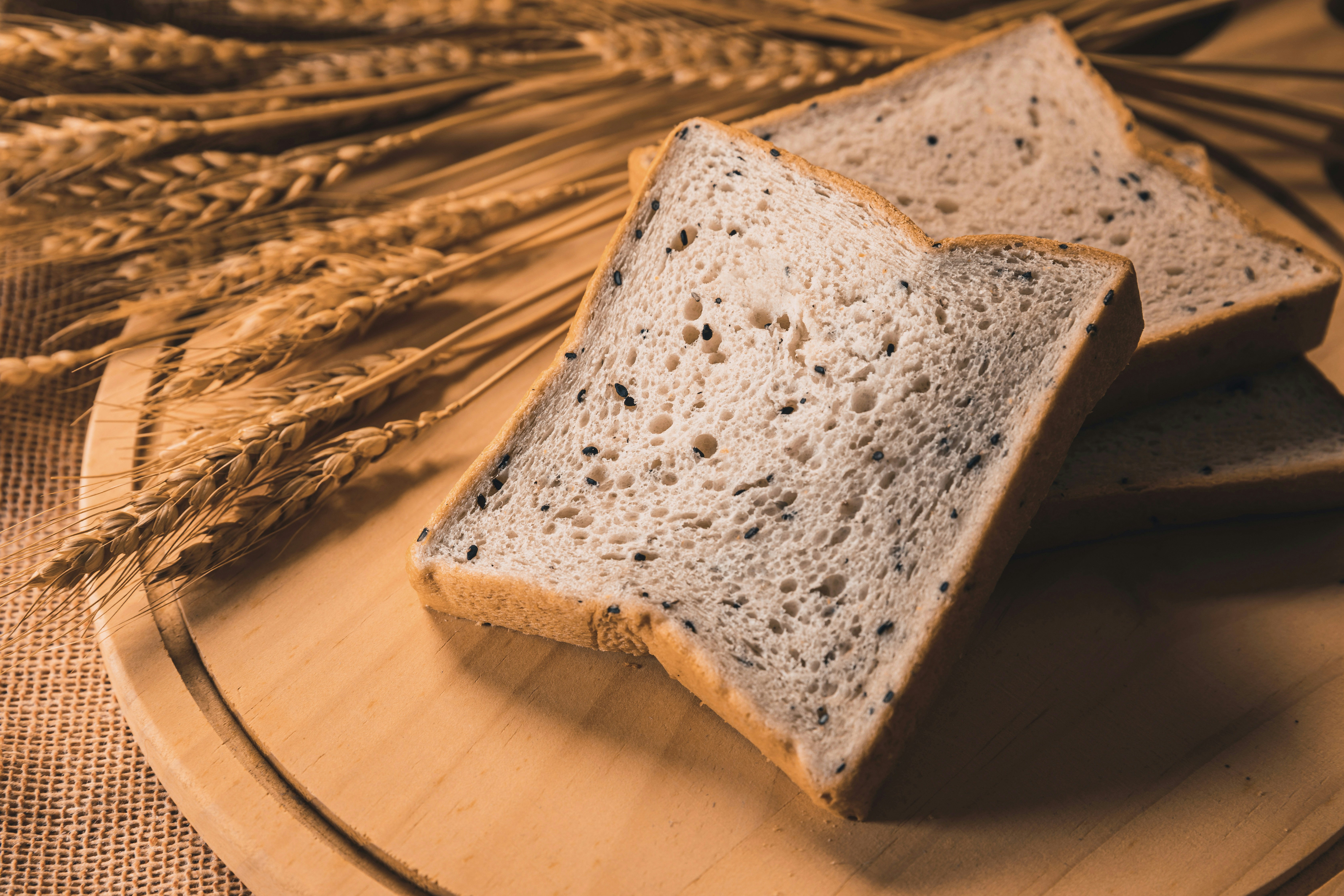 Fotomural Slices of bread with black sesame seeds on a wooden board with wheat stalks