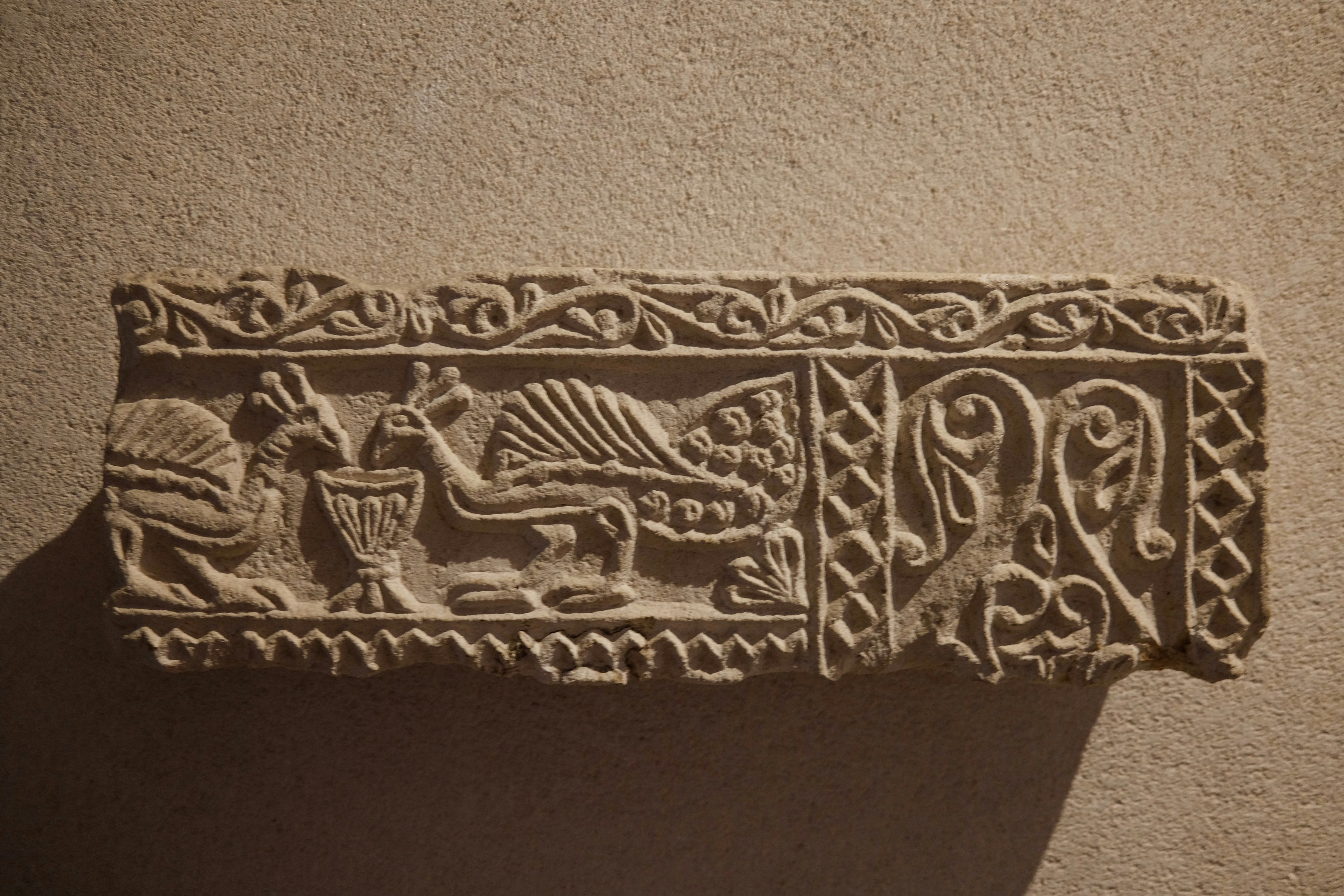 A stone relief carving of two peacocks drinking from a chalice with decorative borders