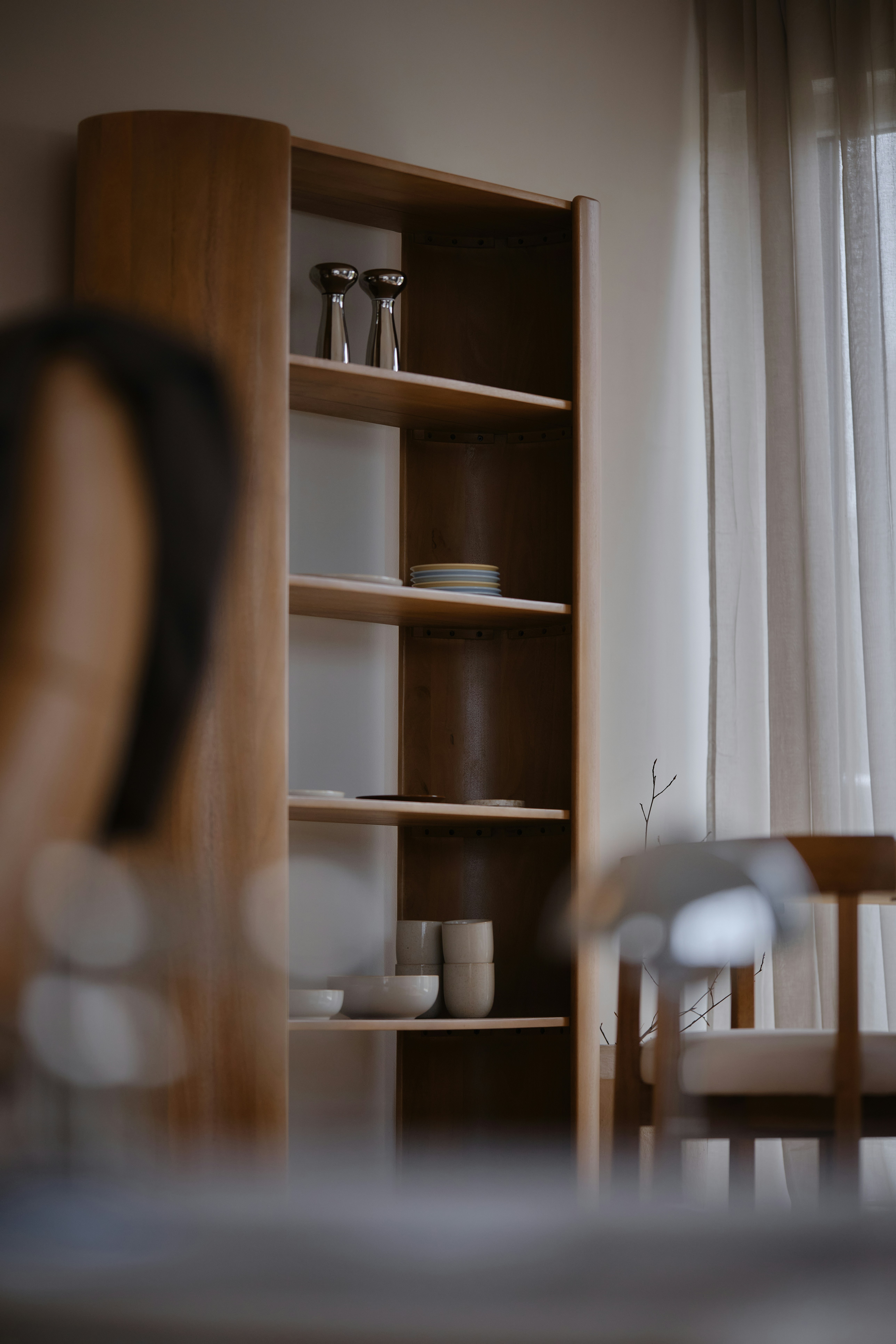 A wooden shelving unit with ceramic bowls and metal shakers in a sunlit room - 相关推荐