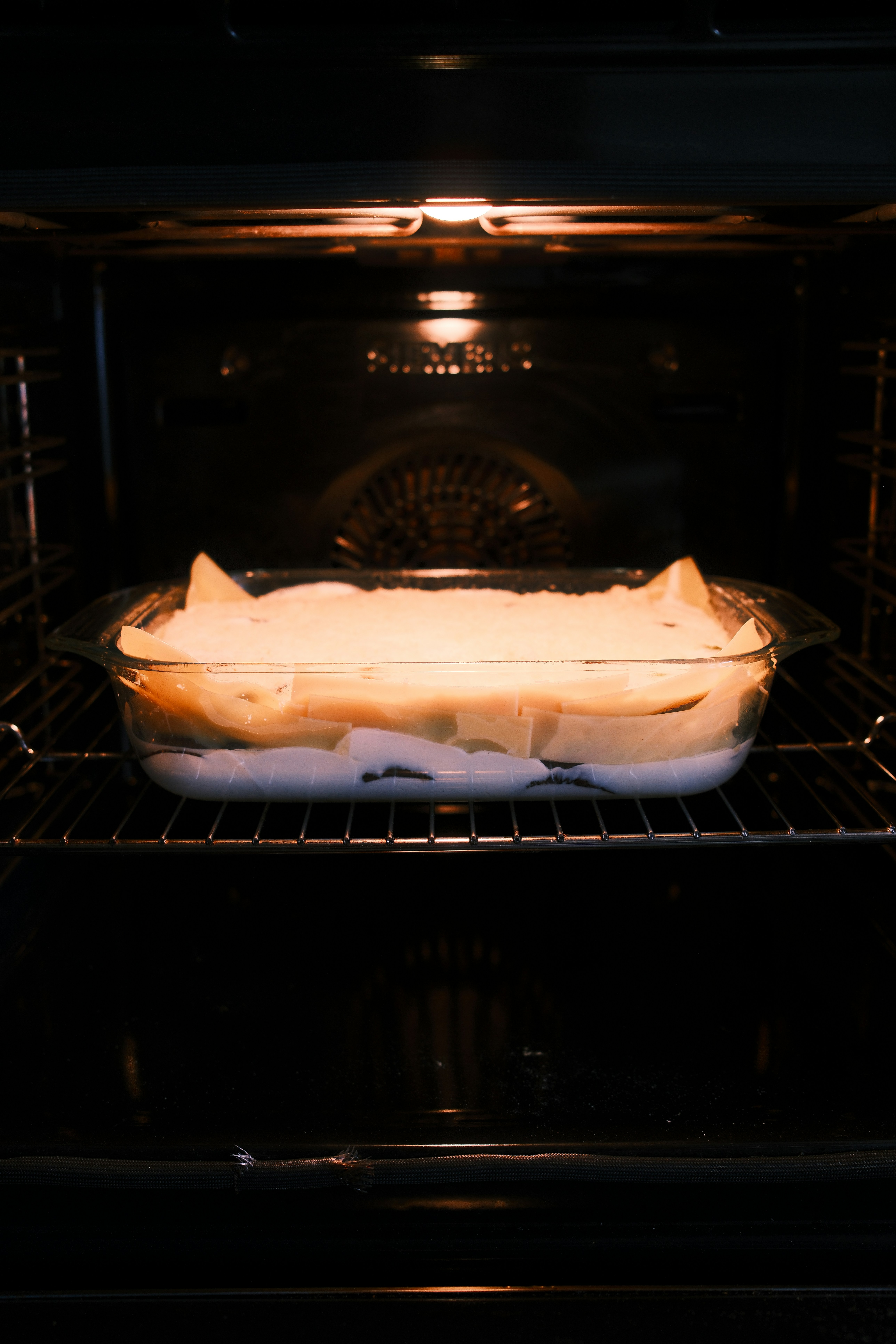 Fotomural A glass baking dish with layered lasagna inside a lit oven