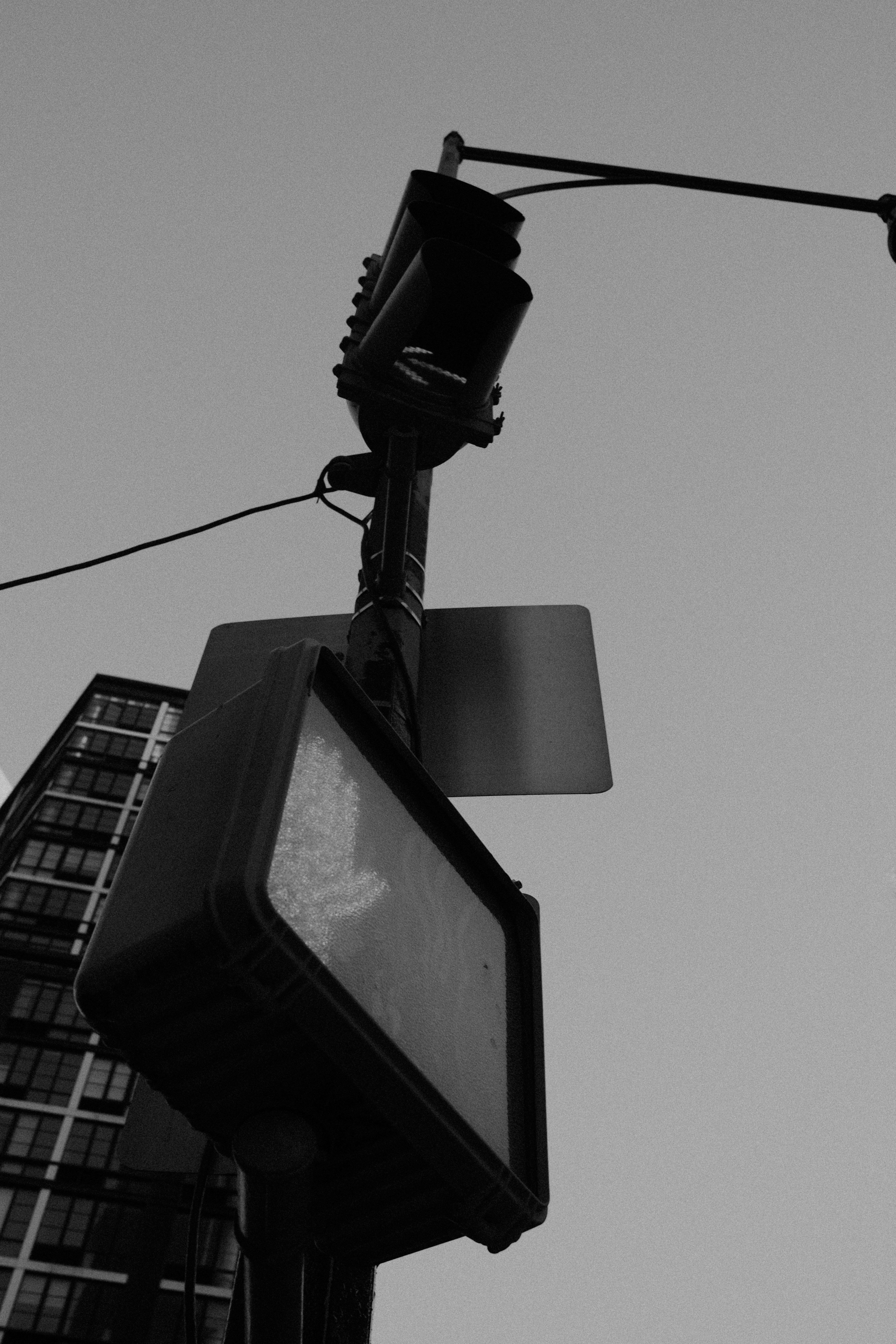 A black and white low angle view of a pedestrian signal and traffic light against a clear sky